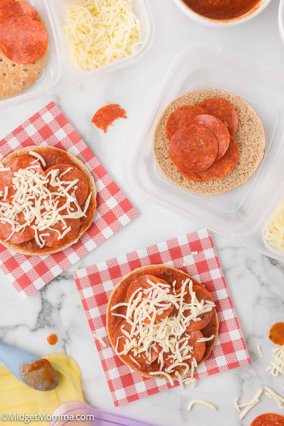 Ingredients for lunchable pizzas, including pepperoni, cheese, sauce, and bread, on a marble surface with napkins.