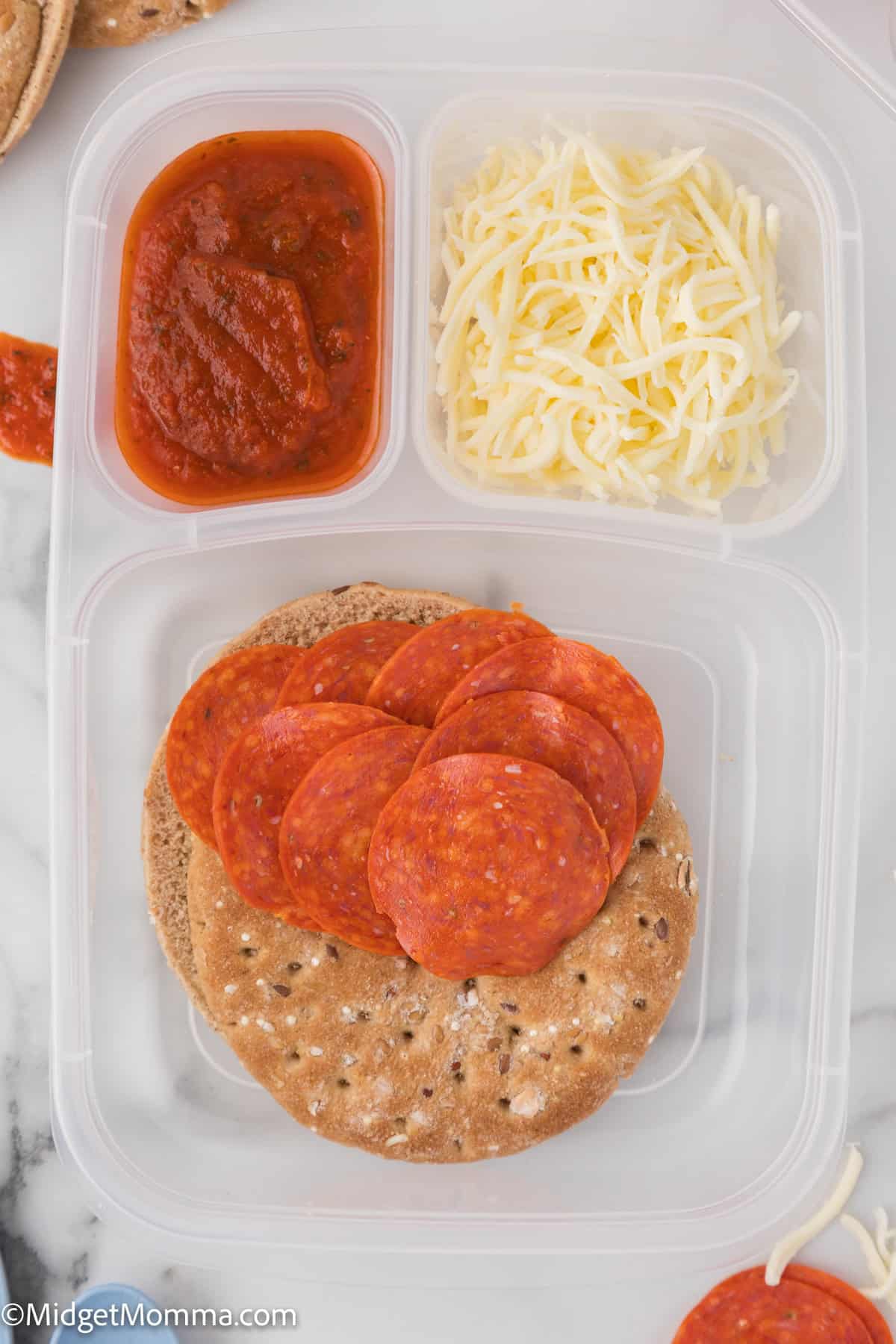 A plastic container with sliced pepperoni, shredded cheese, pizza sauce, and flatbread rounds.