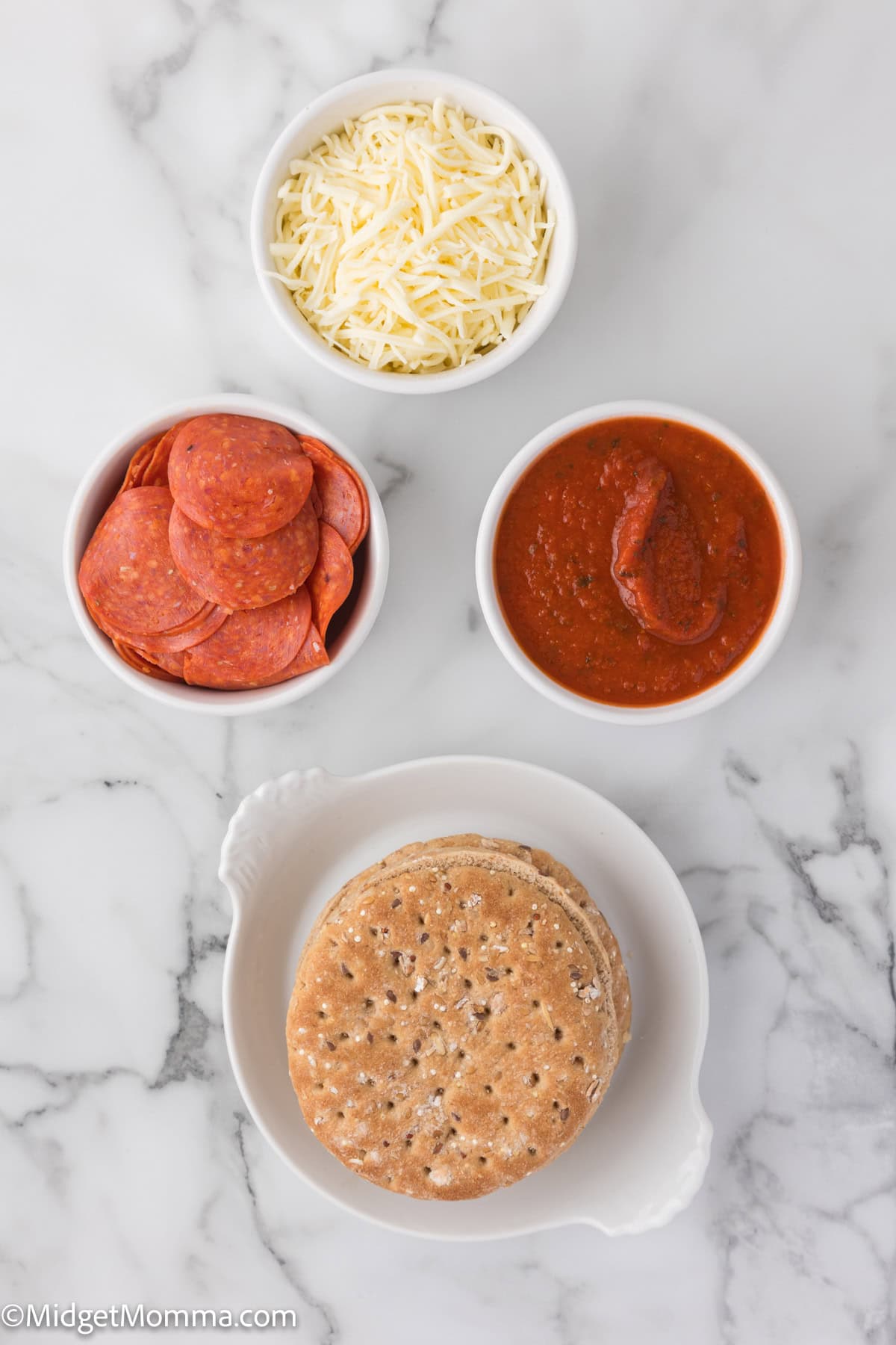 Ingredients for homemade pizza: shredded cheese, pepperoni slices, tomato sauce, and whole wheat sandwich thins on a marble surface.