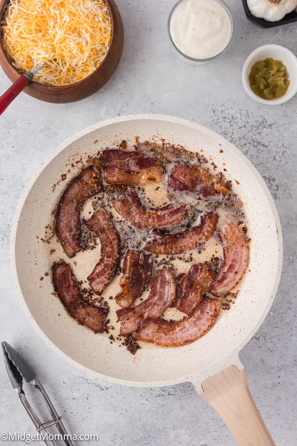 Frying pan with crispy bacon strips. Nearby are bowls with shredded cheese, sour cream. 