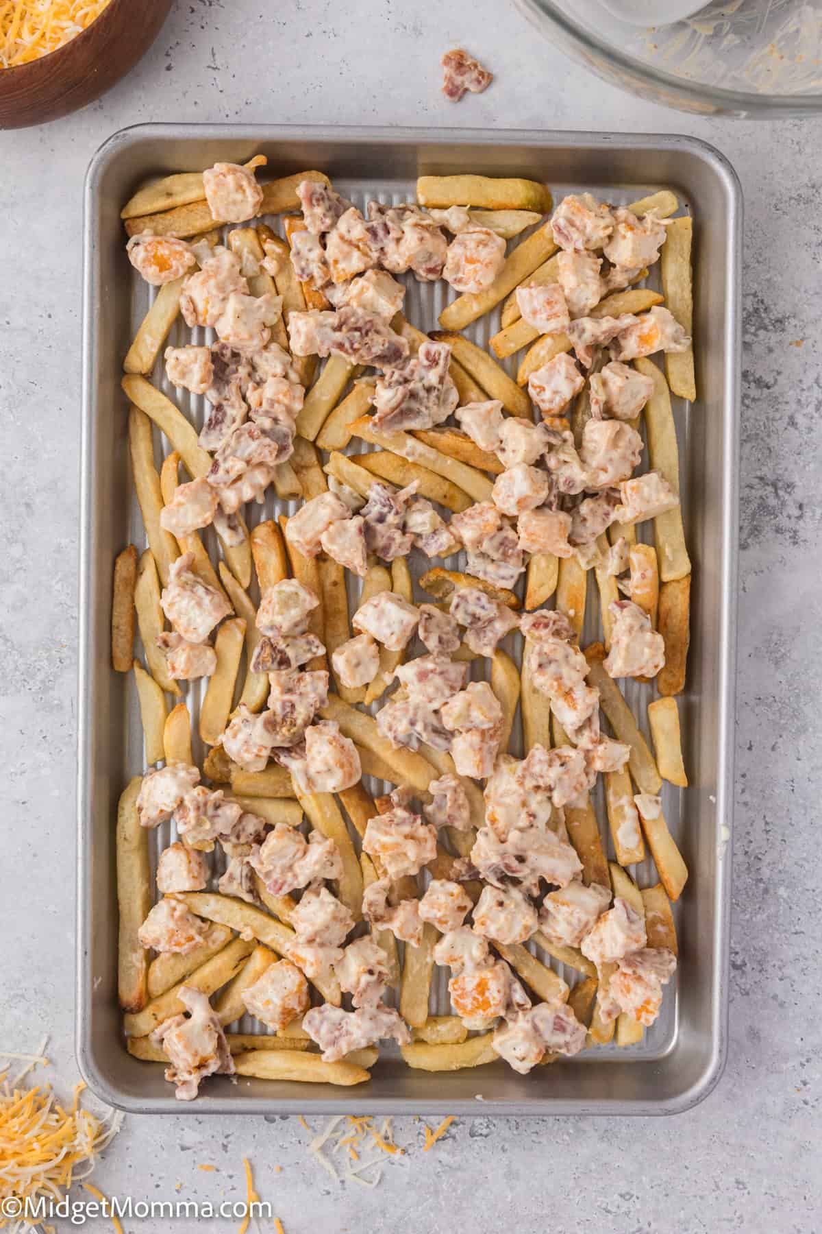 Baked fries topped with diced chicken and melted cheese on a metal tray.