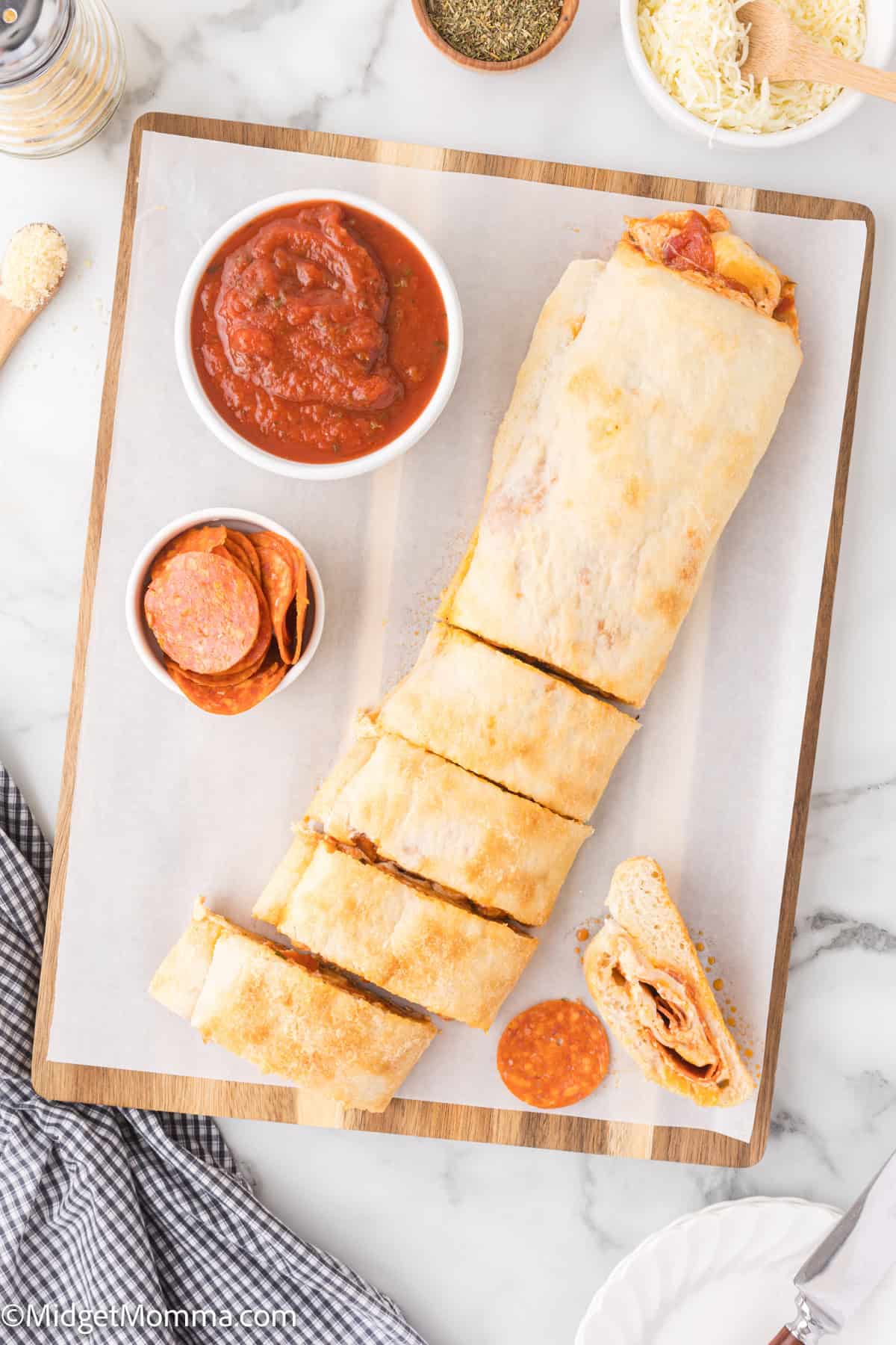 Sliced pepperoni pizza bread on a cutting board with pepperoni, marinara sauce, and grated cheese in small bowls nearby.