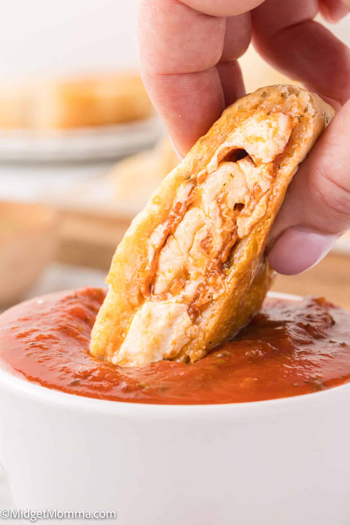 A hand dipping a stuffed pizza bread slice into a bowl of tomato sauce.