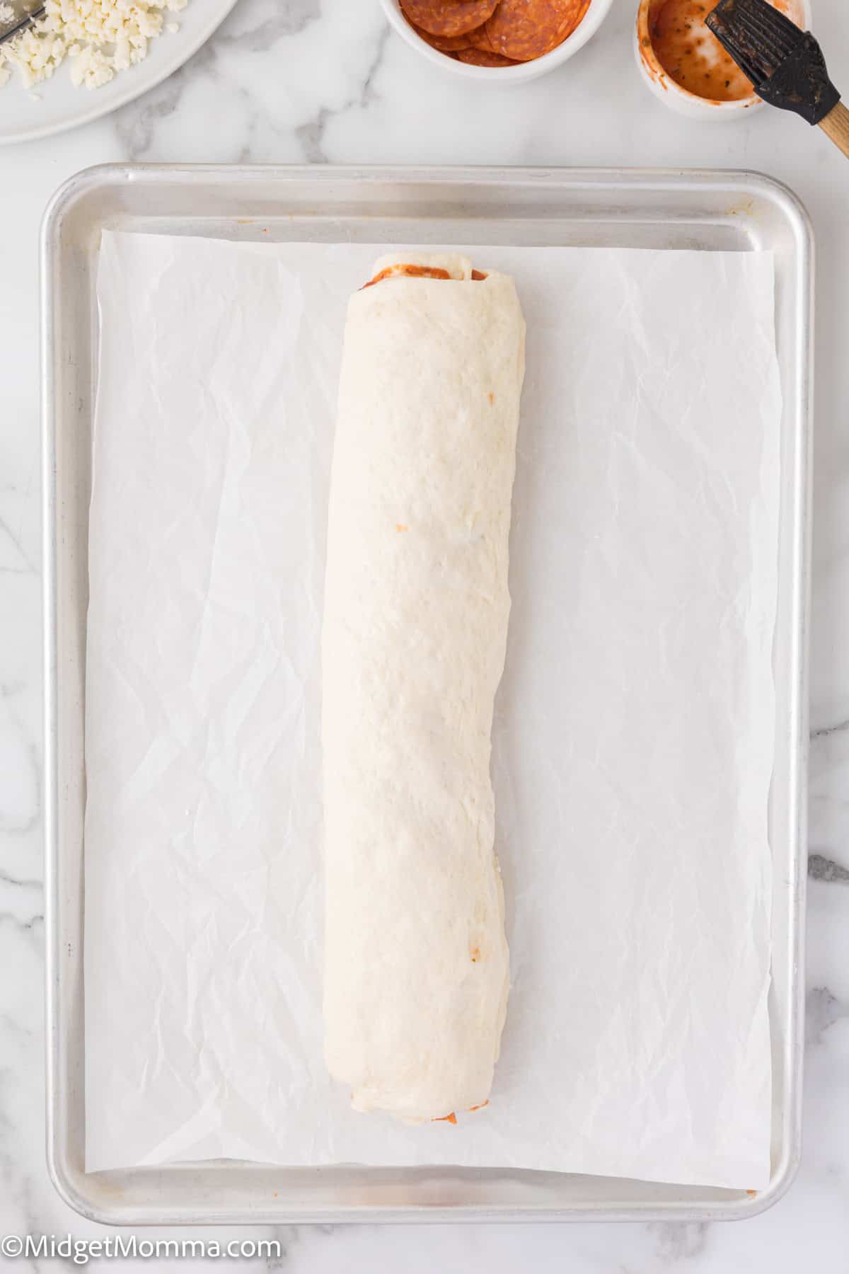 Unbaked rolled dough on parchment-lined baking sheet with small bowls of ingredients in the background.