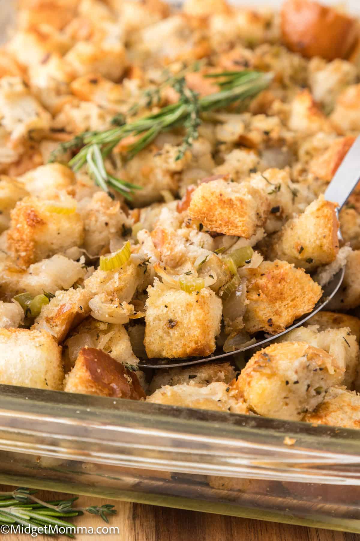 Close-up of a baking dish filled with seasoned stuffing cubes, garnished with fresh rosemary.