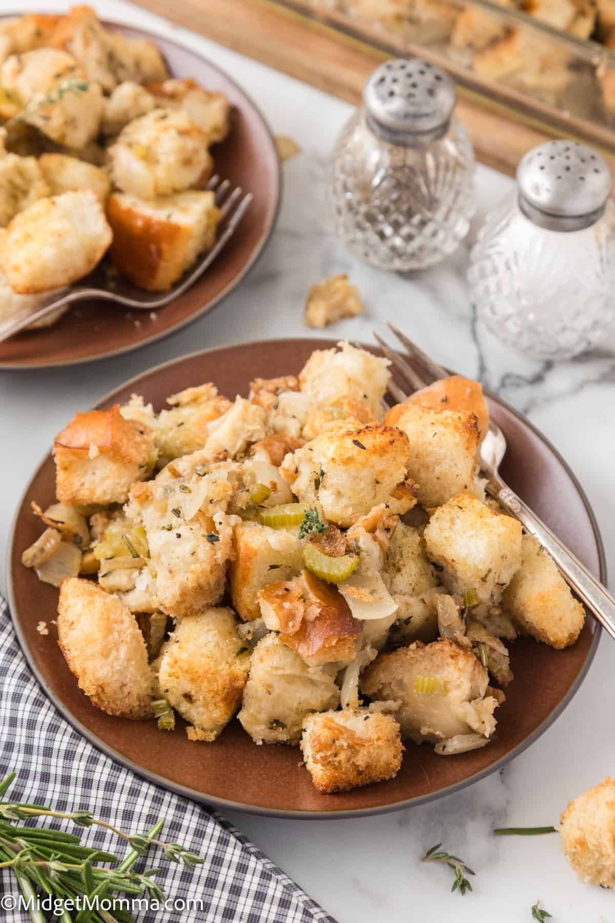 A plate of homemade stuffing with bread cubes, herbs, and vegetables. Two salt and pepper shakers are in the background.