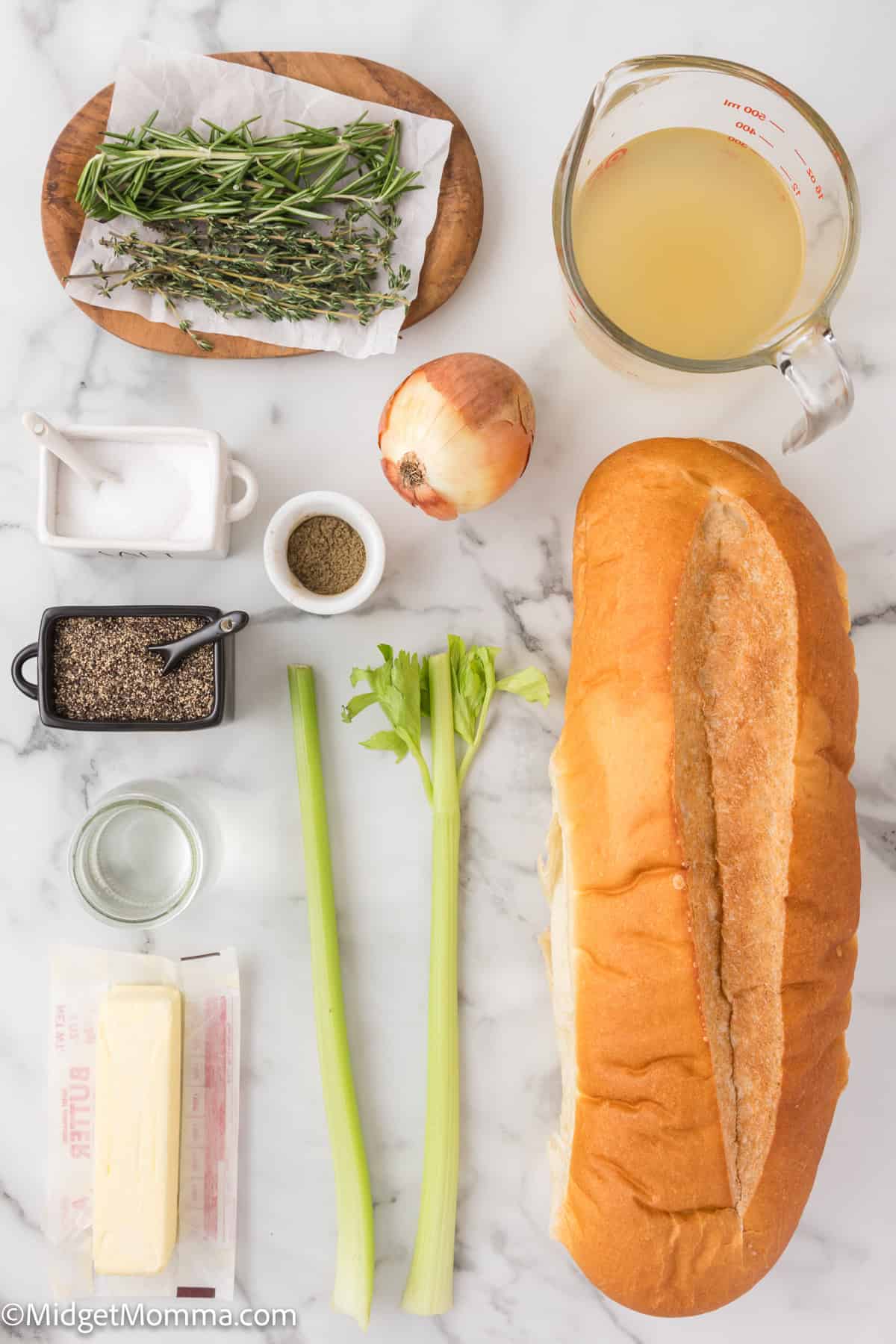 Ingredients on a marble countertop: bread, celery stalks, onion, butter, herbs, black pepper, salt, and chicken broth in a measuring cup.