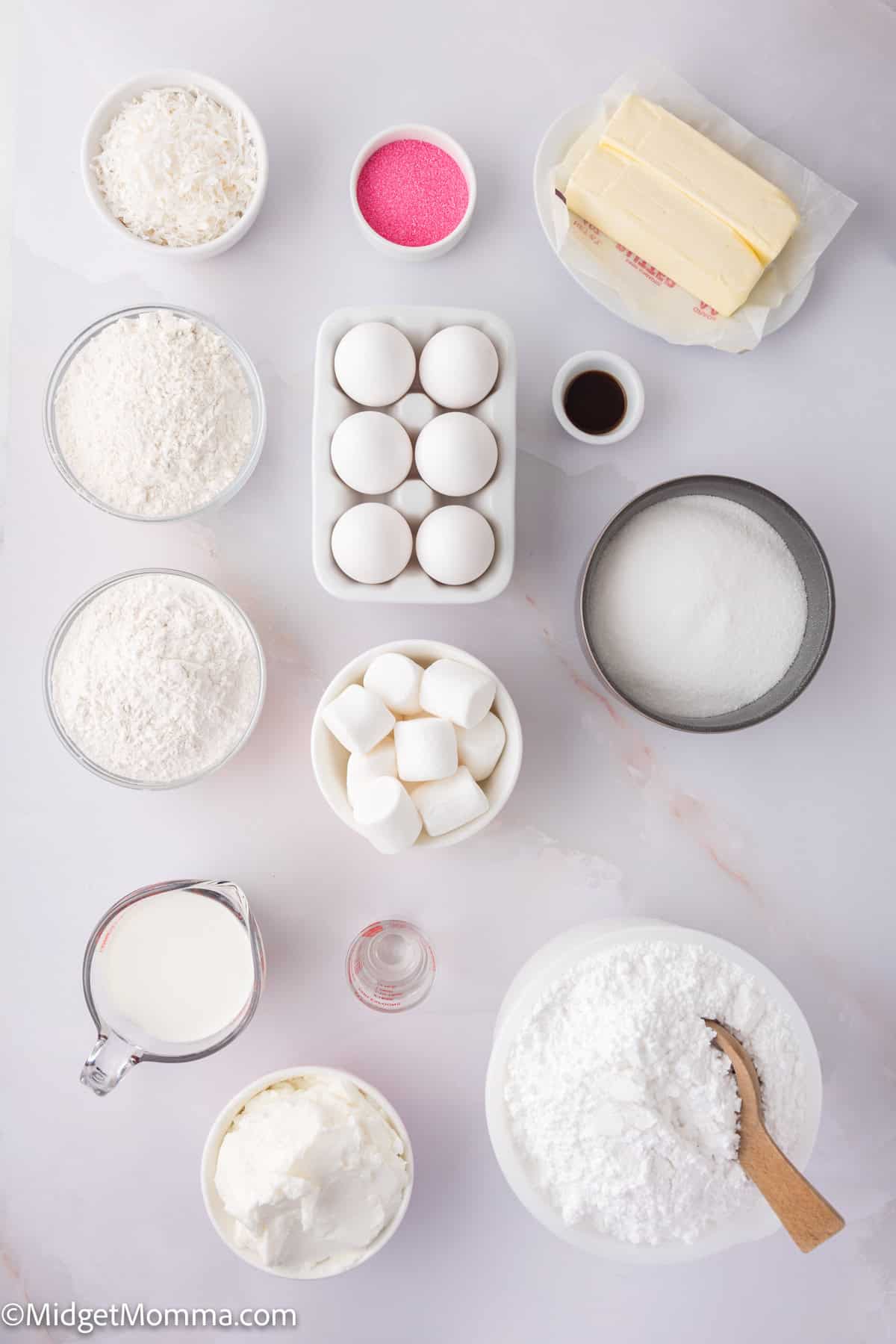 Assorted baking ingredients: eggs, butter, milk, marshmallows, sugar, flour, vanilla, pink sprinkles, and baking powder arranged on a marble surface.