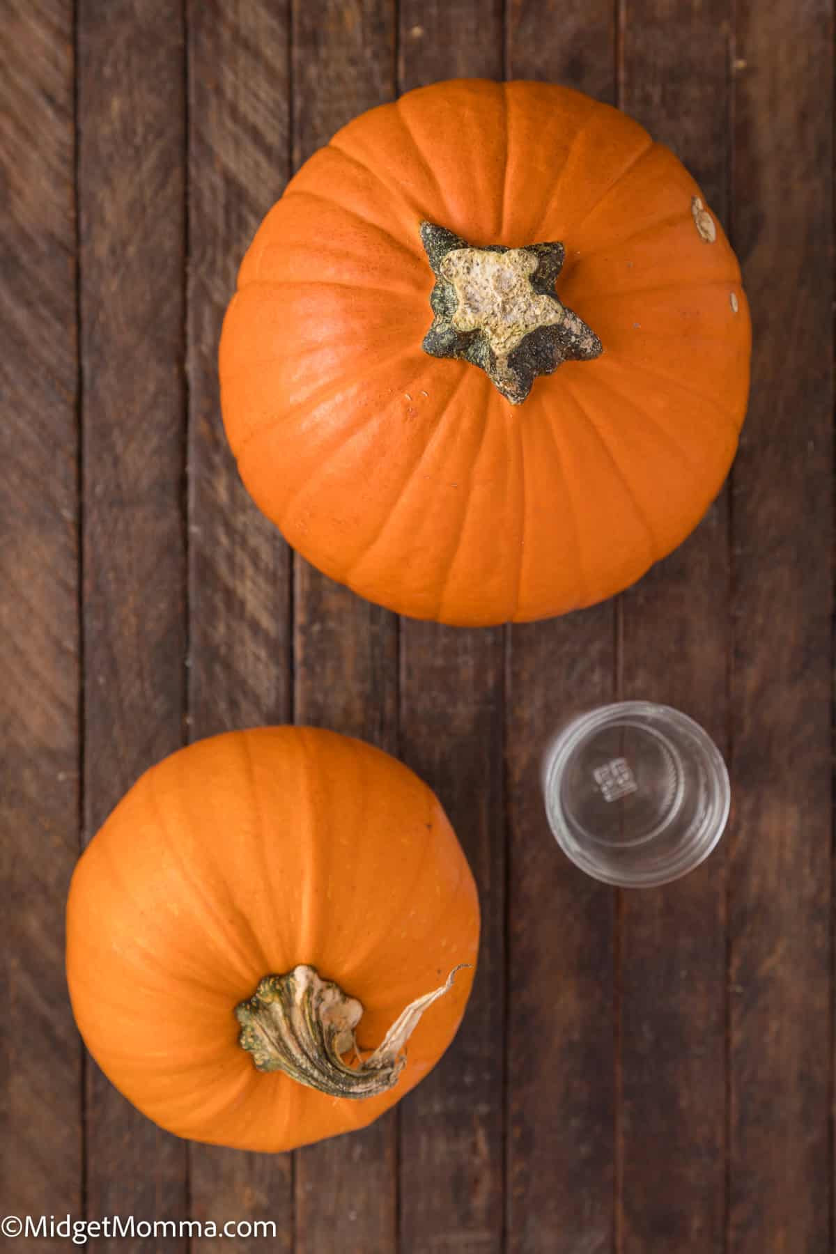 Two orange pumpkins and an empty glass on a wooden surface.