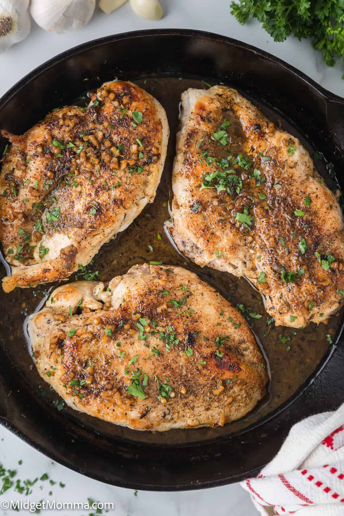 A cast iron skillet containing three seasoned chicken breasts.