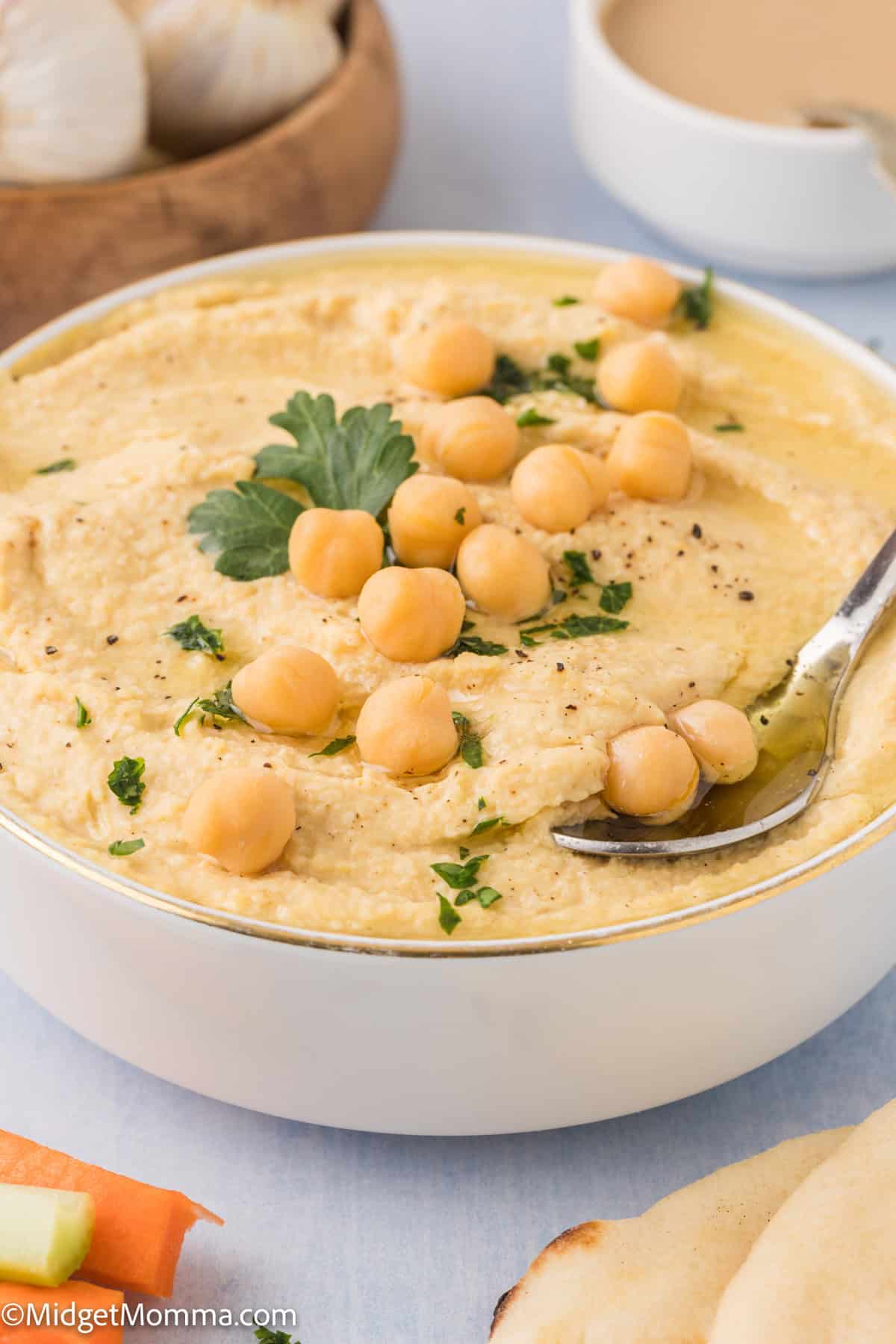 A bowl of hummus garnished with chickpeas and parsley, with a spoon in it.