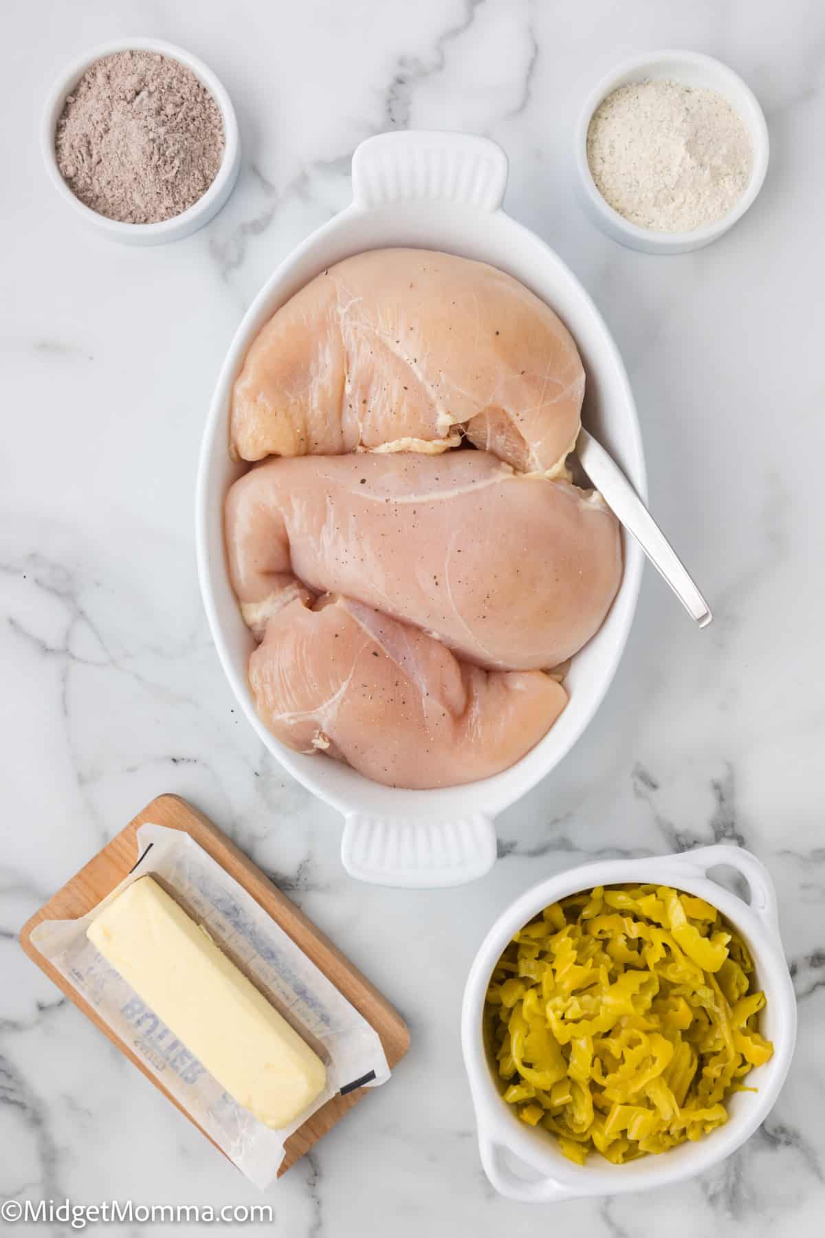 Slow Cooker Mississippi Chicken Recipe ingredients - Raw chicken breasts in a white dish, surrounded by ingredients including flour, spices, butter, and sliced pickles on a marble countertop.