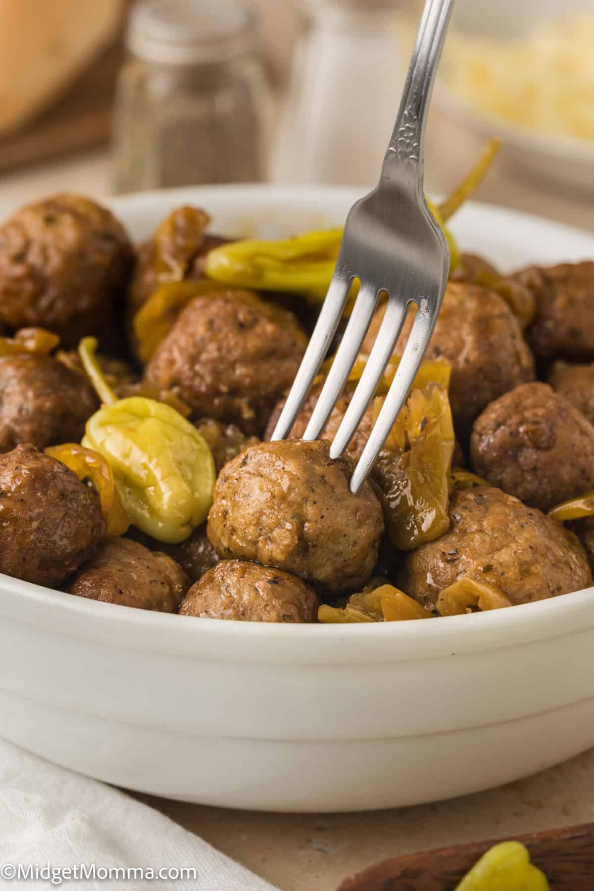 A bowl of cooked meatballs and sliced peppers. A fork is piercing one of the meatballs.