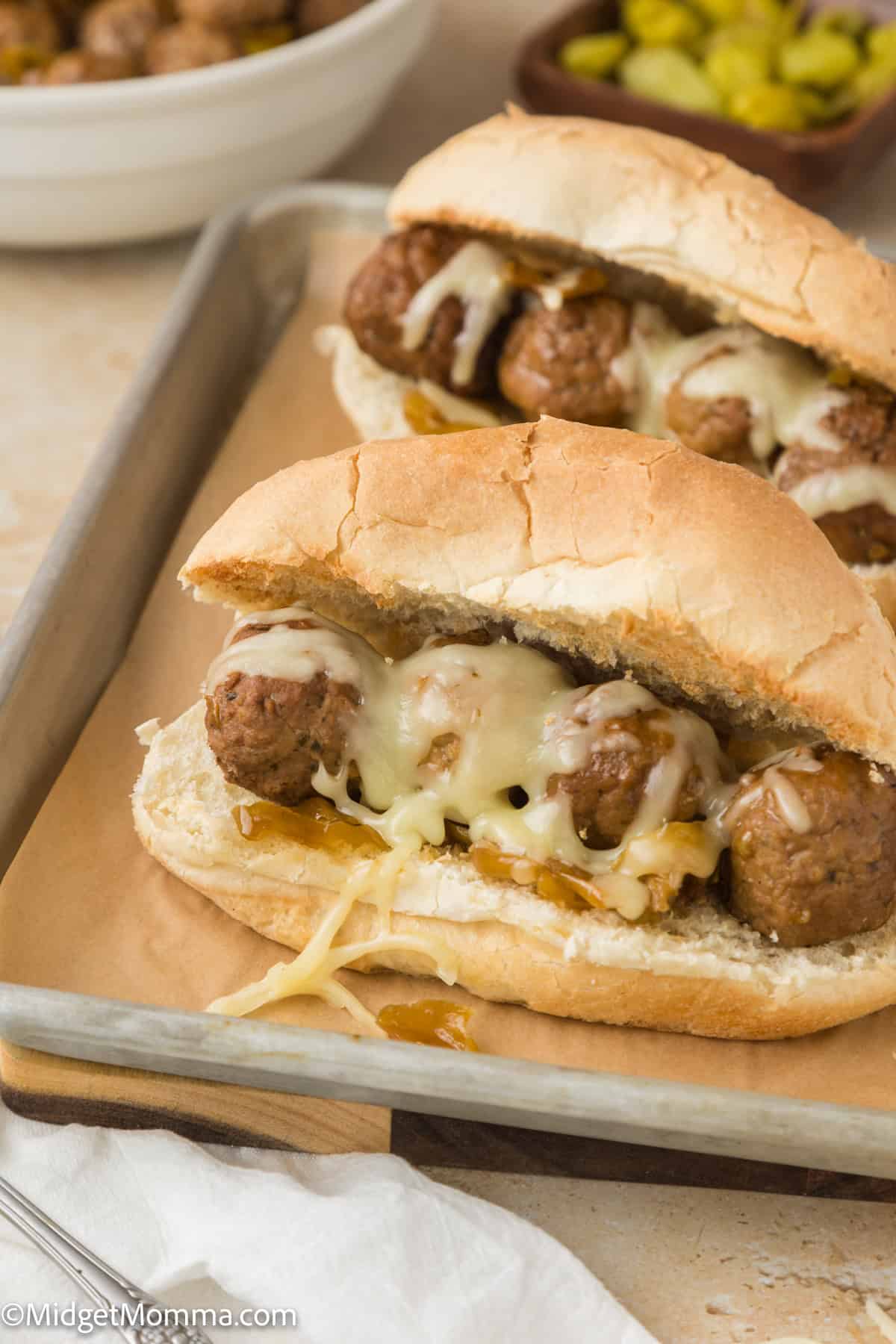 Two meatball subs topped with melted cheese are placed on a baking sheet.