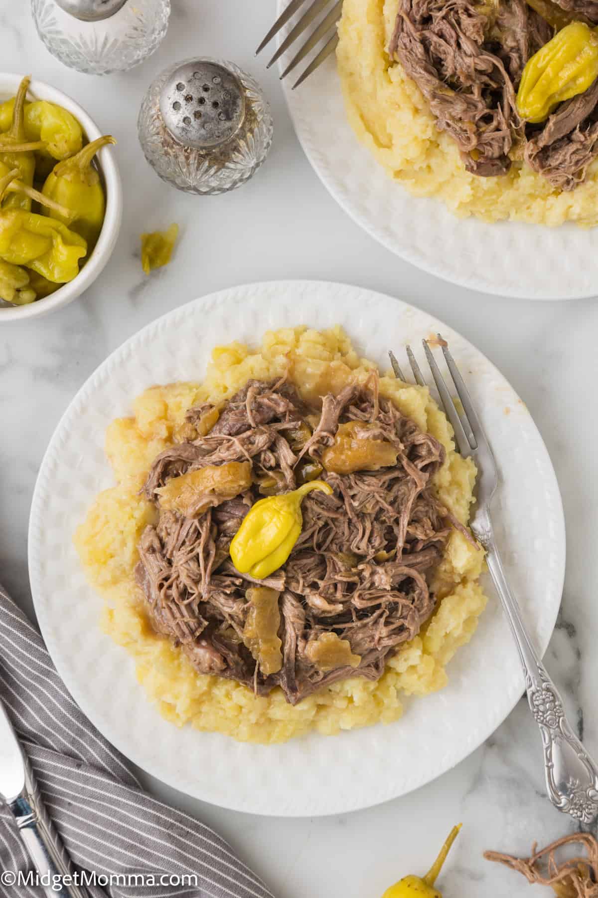 A plate of shredded beef served on mashed potatoes with peppers on top.