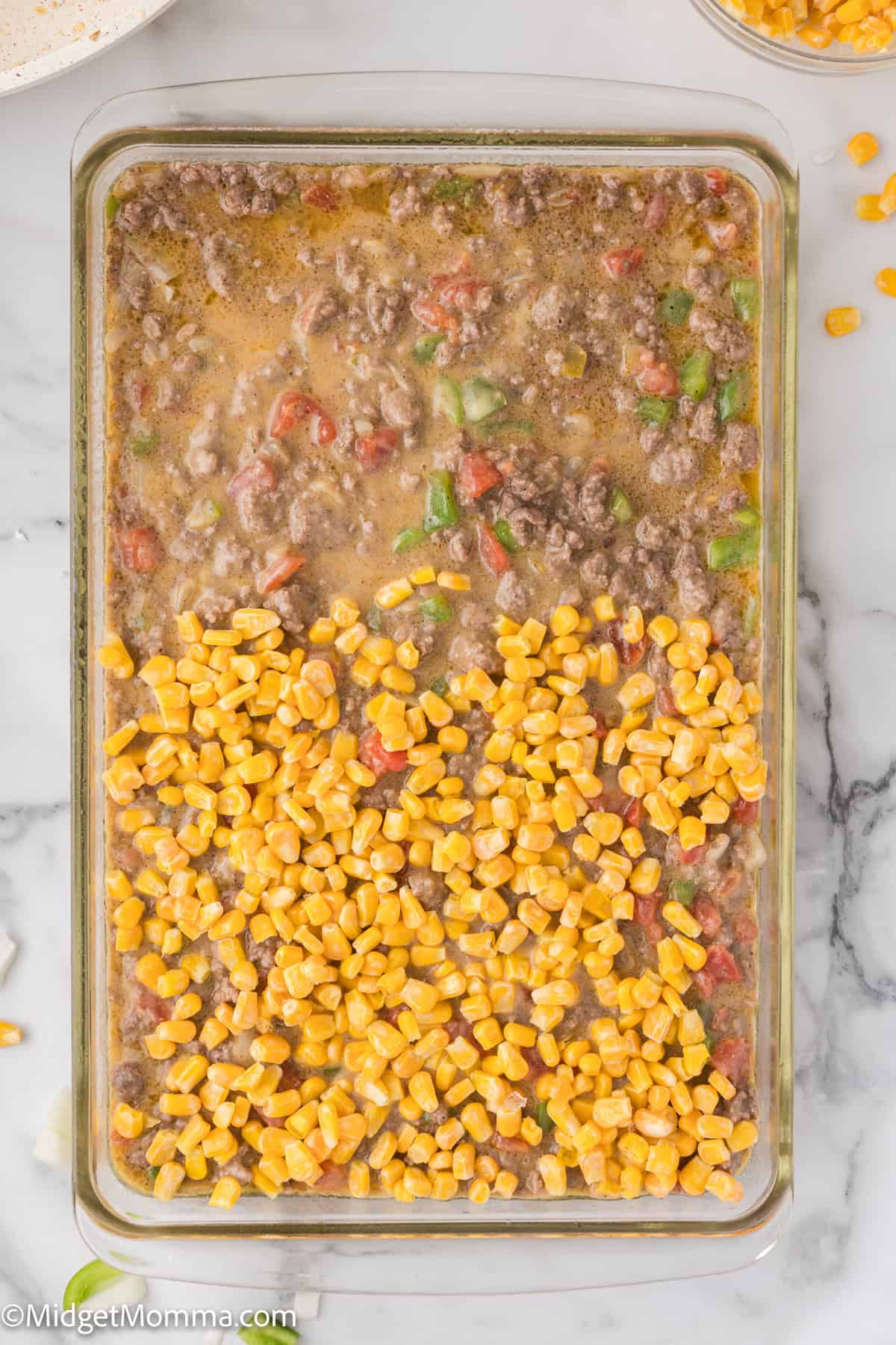 A glass baking dish filled with a mixture of ground beef, chopped vegetables, and topped with a layer of yellow corn.