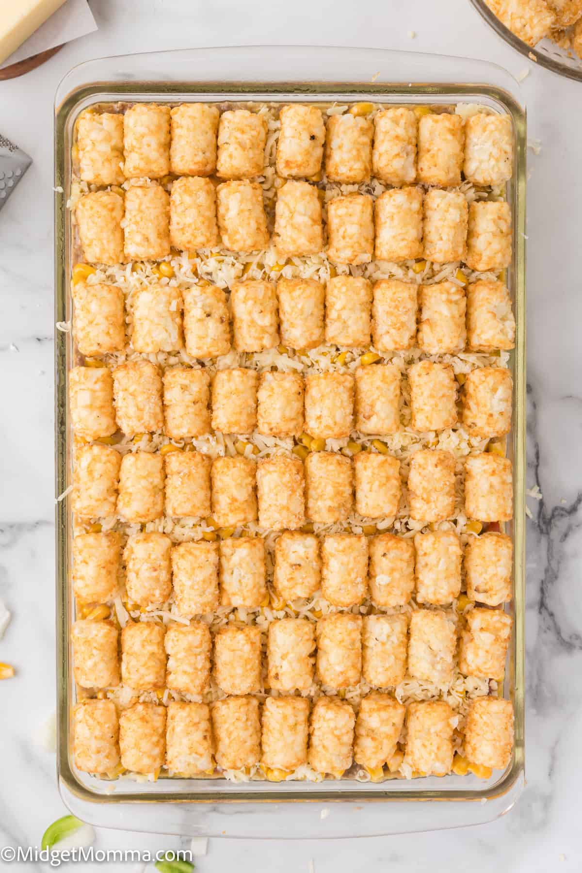 A rectangular casserole dish filled with neatly arranged rows of tater tots on top of a baked mixture, likely a tater tot casserole.