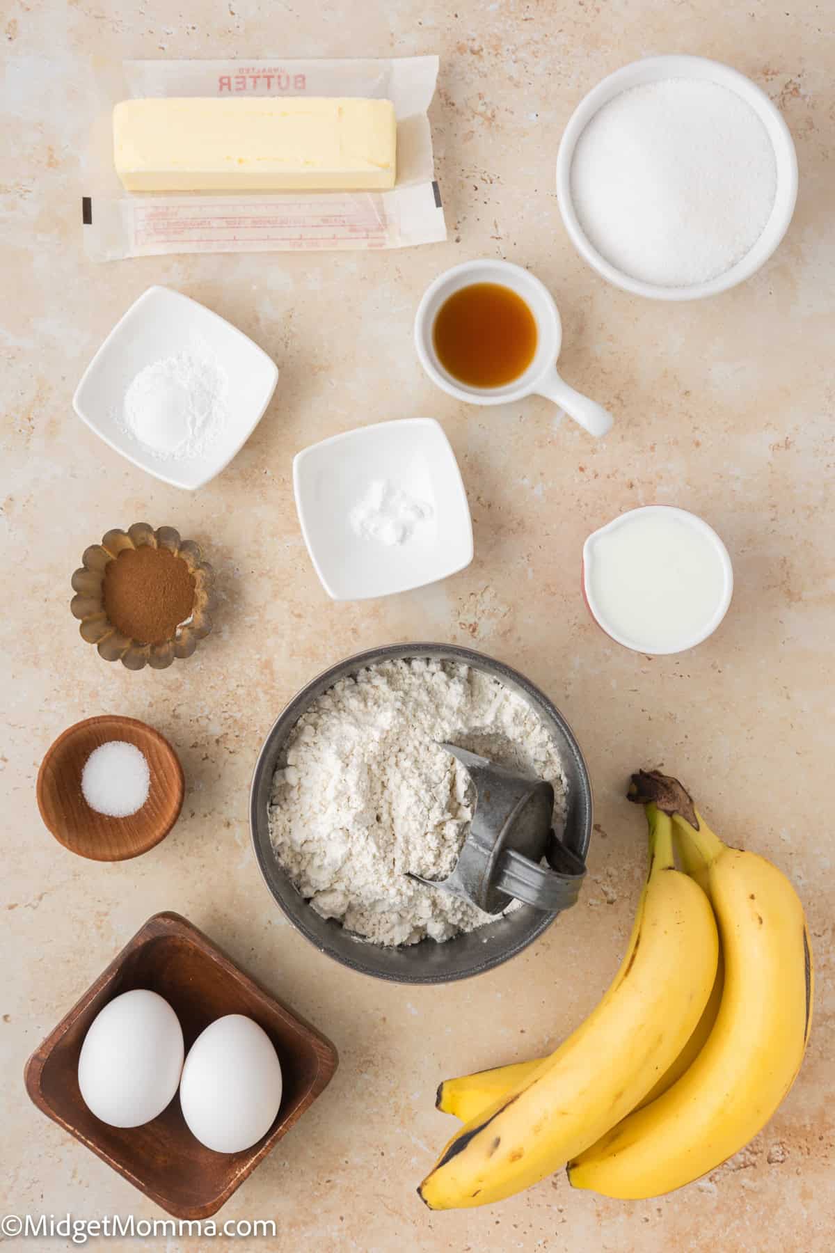 Ingredients laid out on a beige surface include bananas, eggs, flour, sugar, butter, vanilla extract, baking soda, baking powder, salt, and milk.