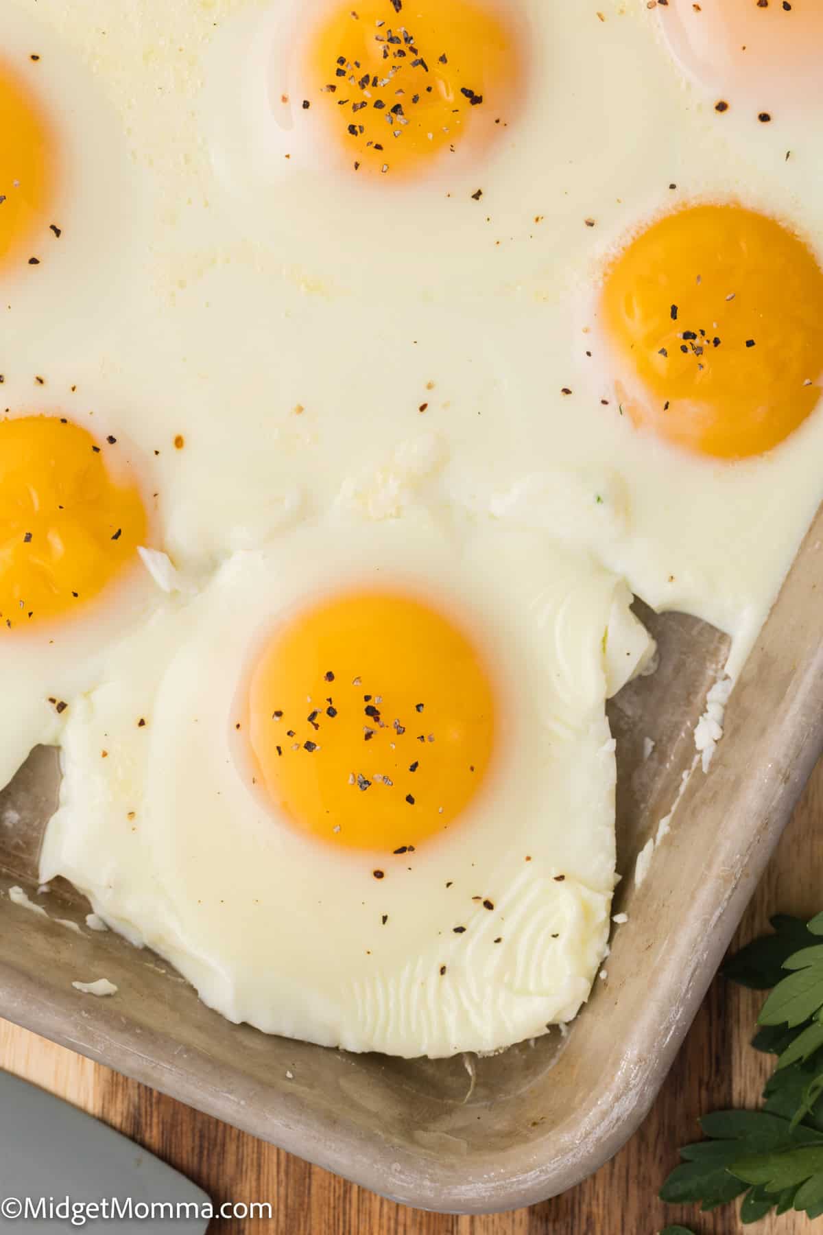 A baking sheet with several baked eggs, featuring bright yellow yolks and seasoned with black pepper.