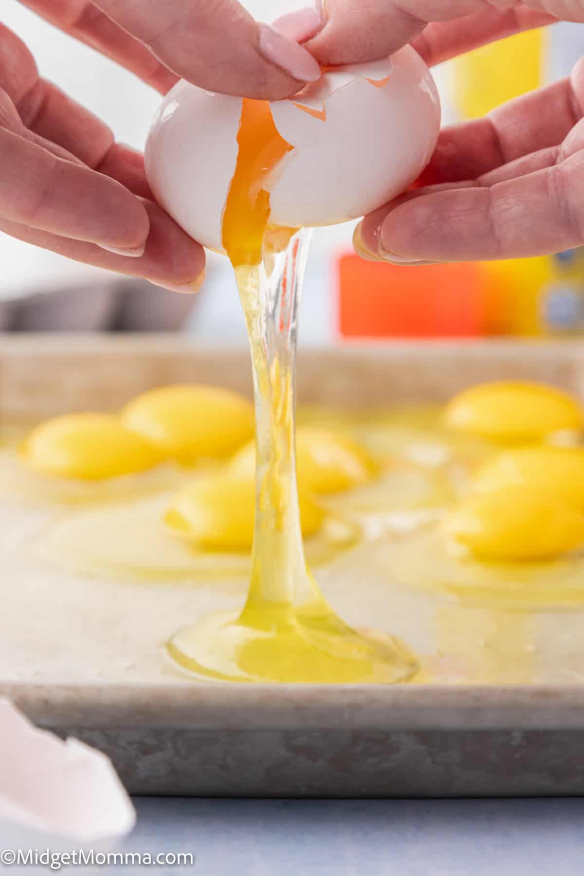 Hands cracking an egg, with the yolk and white flowing into a pan. Multiple cracked eggs already present in the background.
