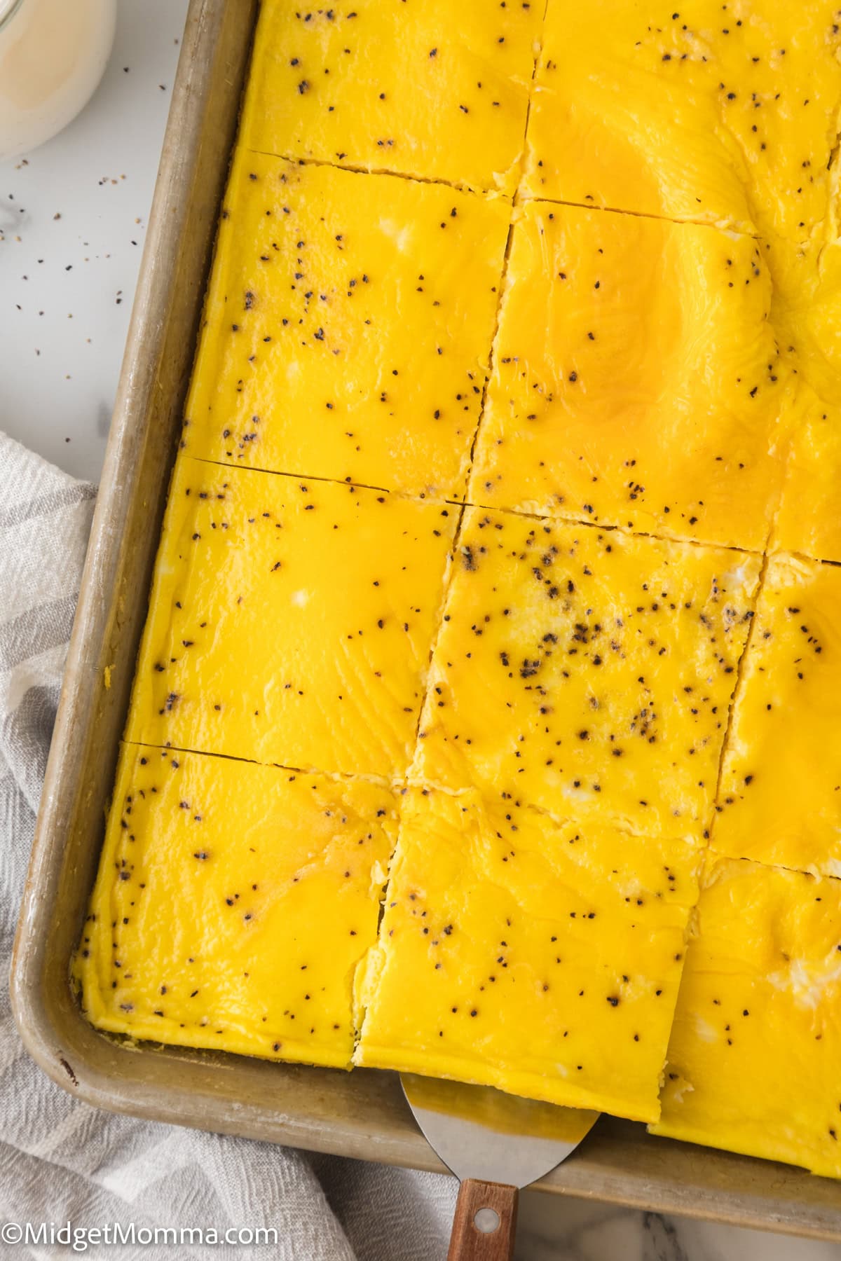 A rectangular baking tray with baked eggs cut into portions. A spatula is lifting one square from the tray.