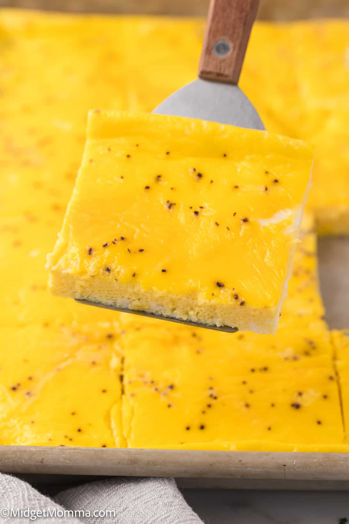 A spatula holds a square slice of sheet pan scrambled eggs.