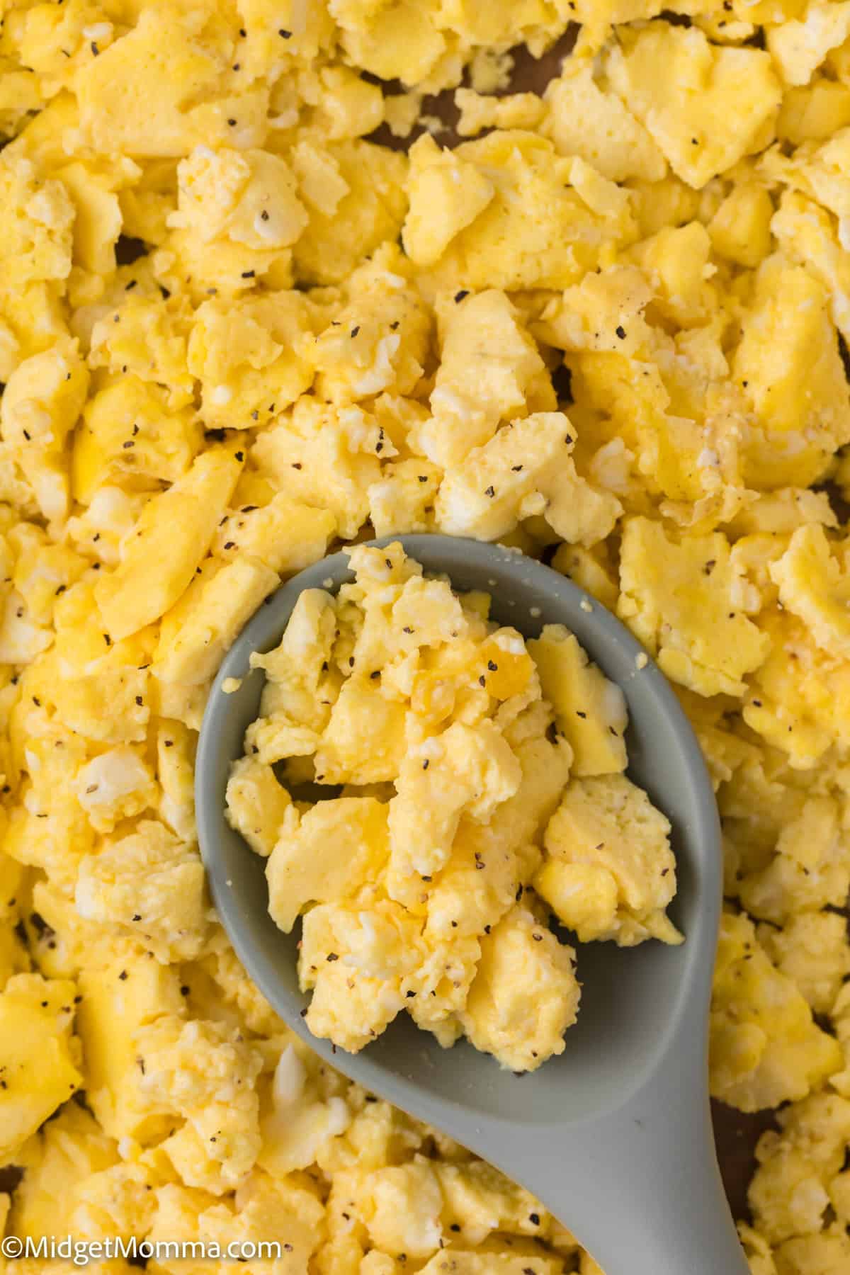 Close-up of scrambled eggs with black pepper, with a gray spoon scooping some eggs from the dish.