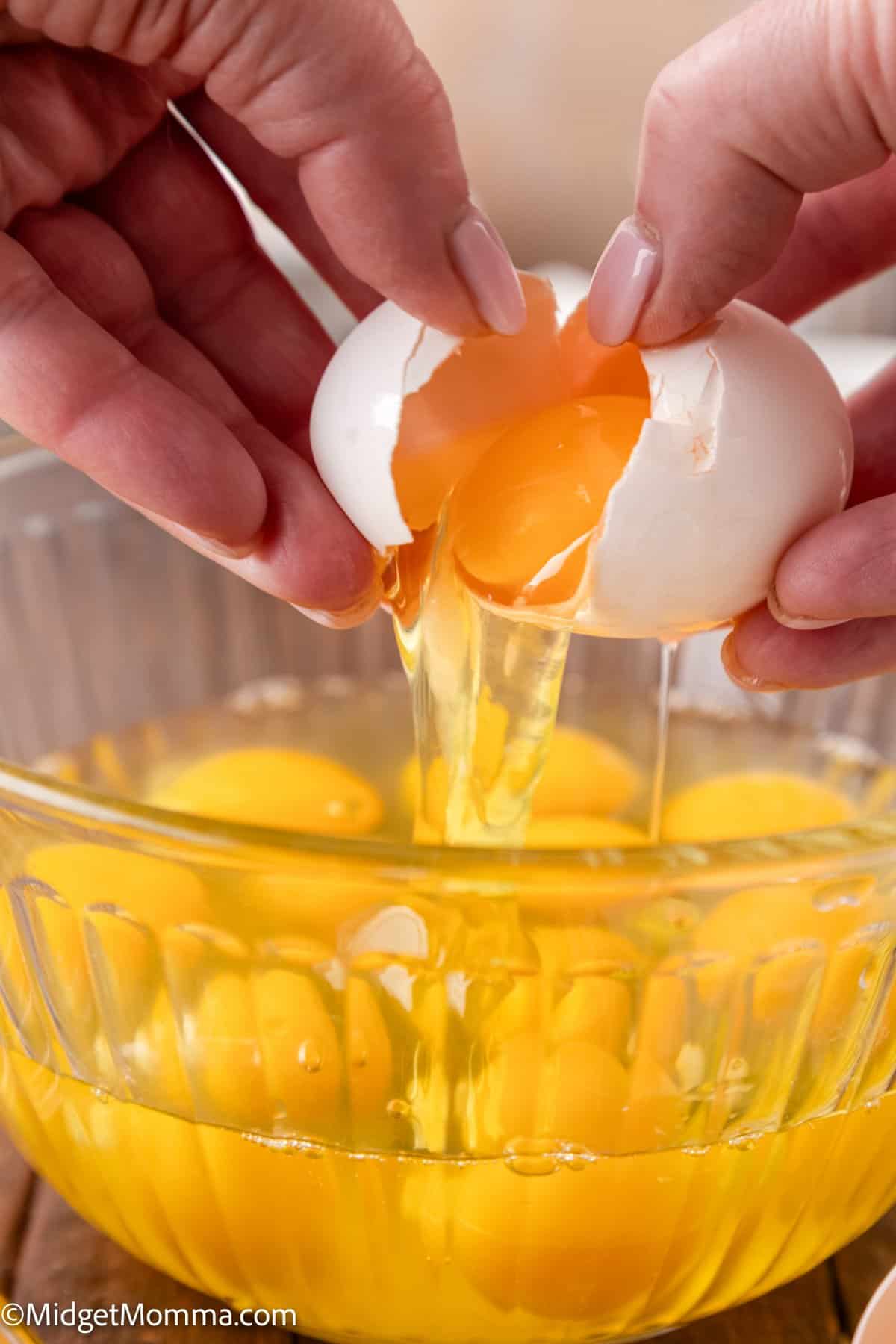 Hands cracking an egg into a glass bowl containing other cracked eggs.