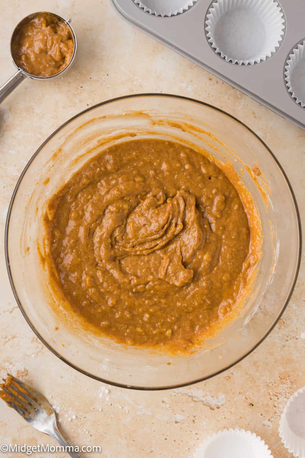 A clear glass bowl on the counter top filled with pumpkin banana muffin batter.