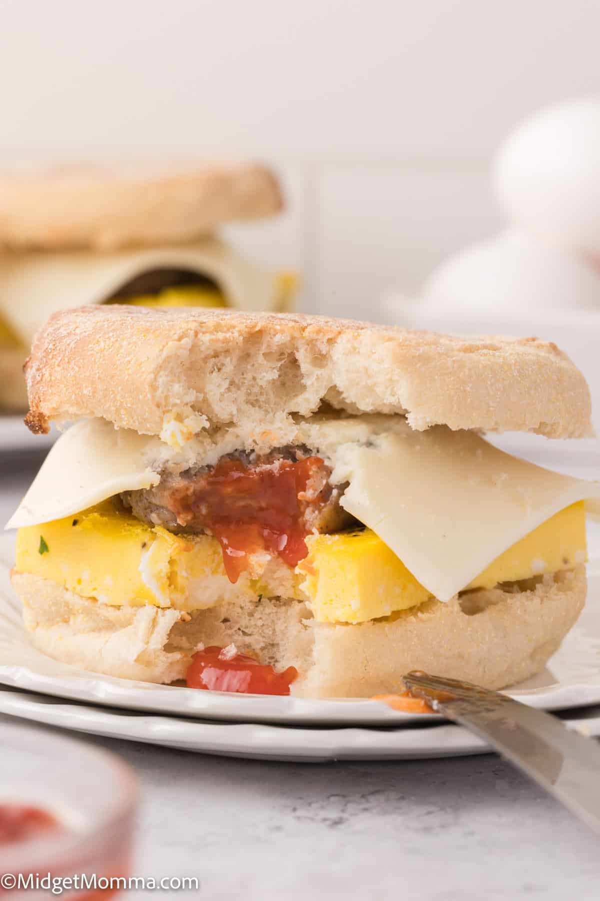 A breakfast sandwich on an English muffin with egg, cheese, and ketchup, with a bite taken out of it.