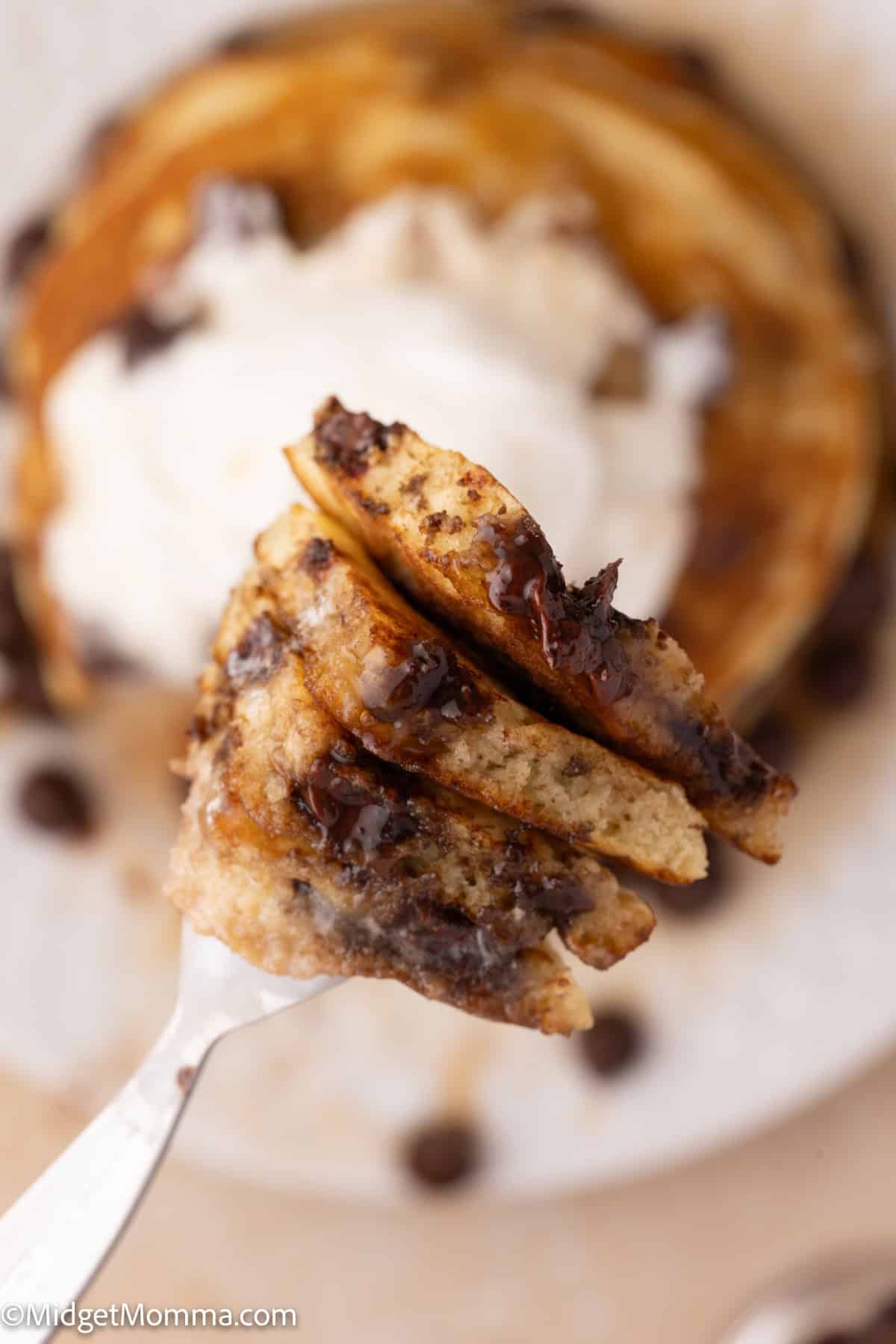 Close-up of a fork holding a piece of chocolate chip pancake with whipped cream in the background.