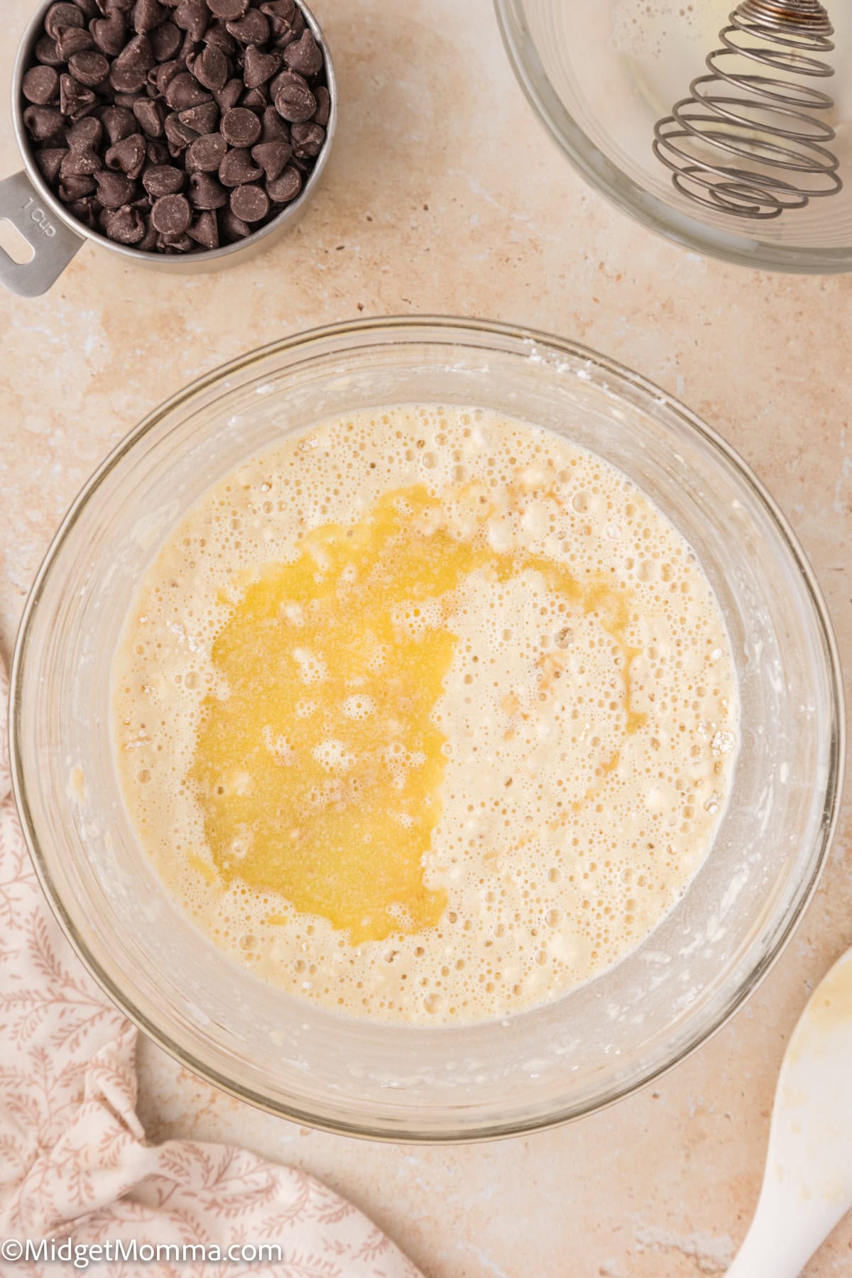 A mixing bowl with a partially mixed batter, a cup of chocolate chips, and a whisk.