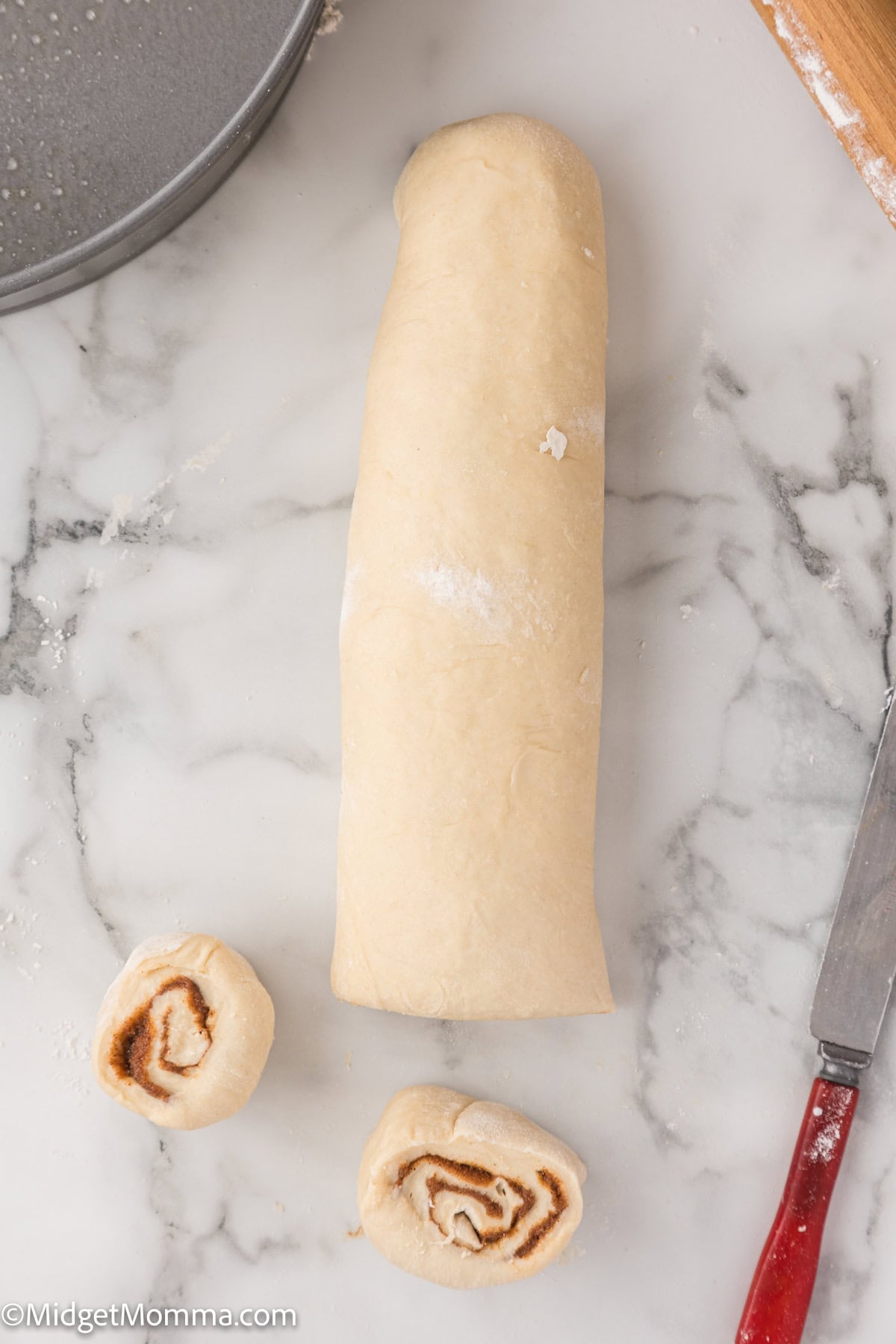 Rolled dough on a marble surface with two sliced pieces next to a knife.