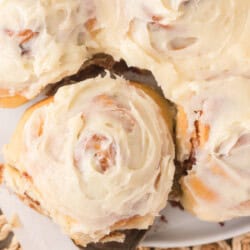 A close-up of frosted cinnamon rolls, with one being lifted by a spatula.