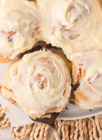 A close-up of frosted cinnamon rolls, with one being lifted by a spatula.