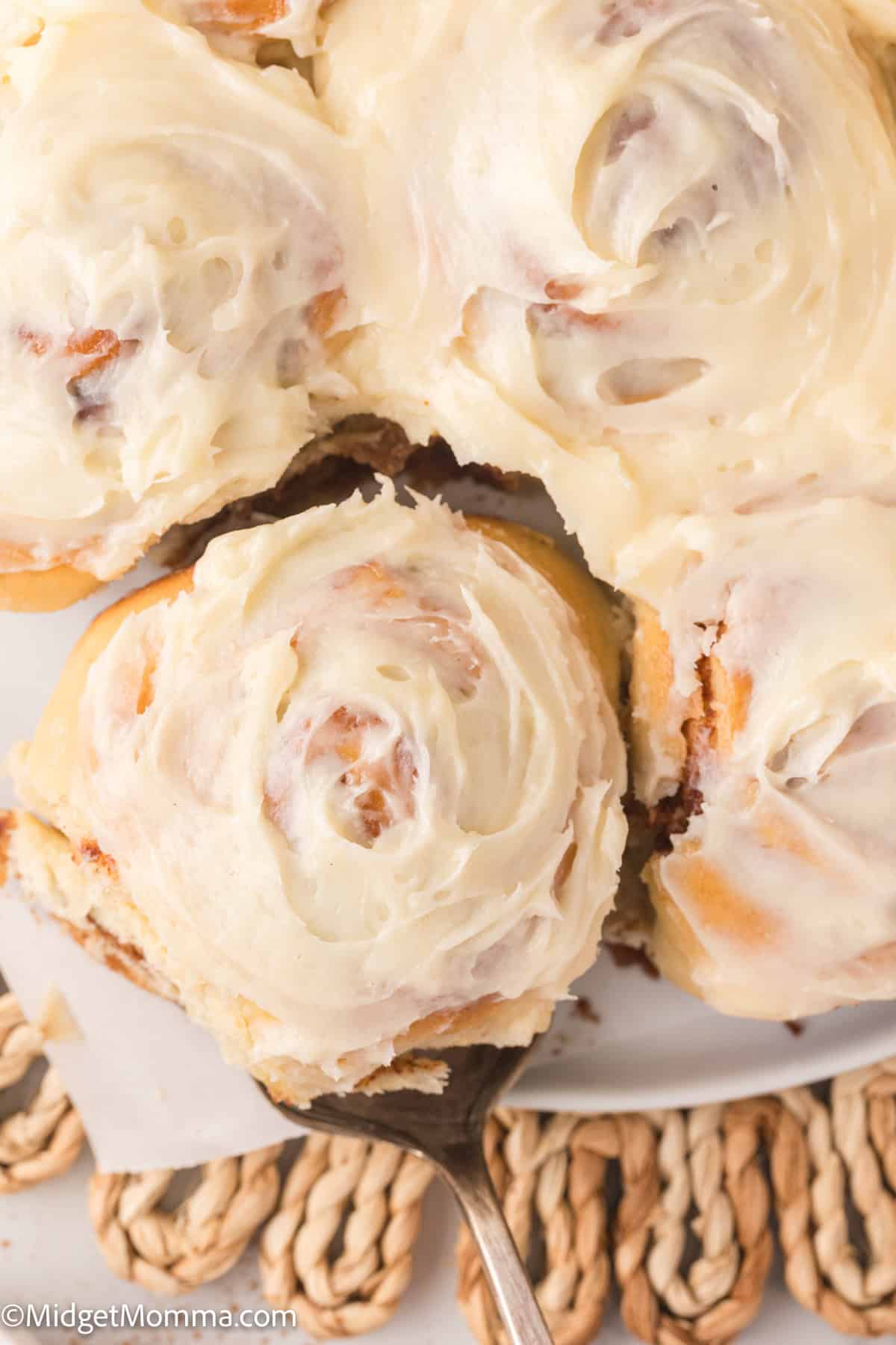 A close-up of frosted cinnamon rolls, with one being lifted by a spatula.