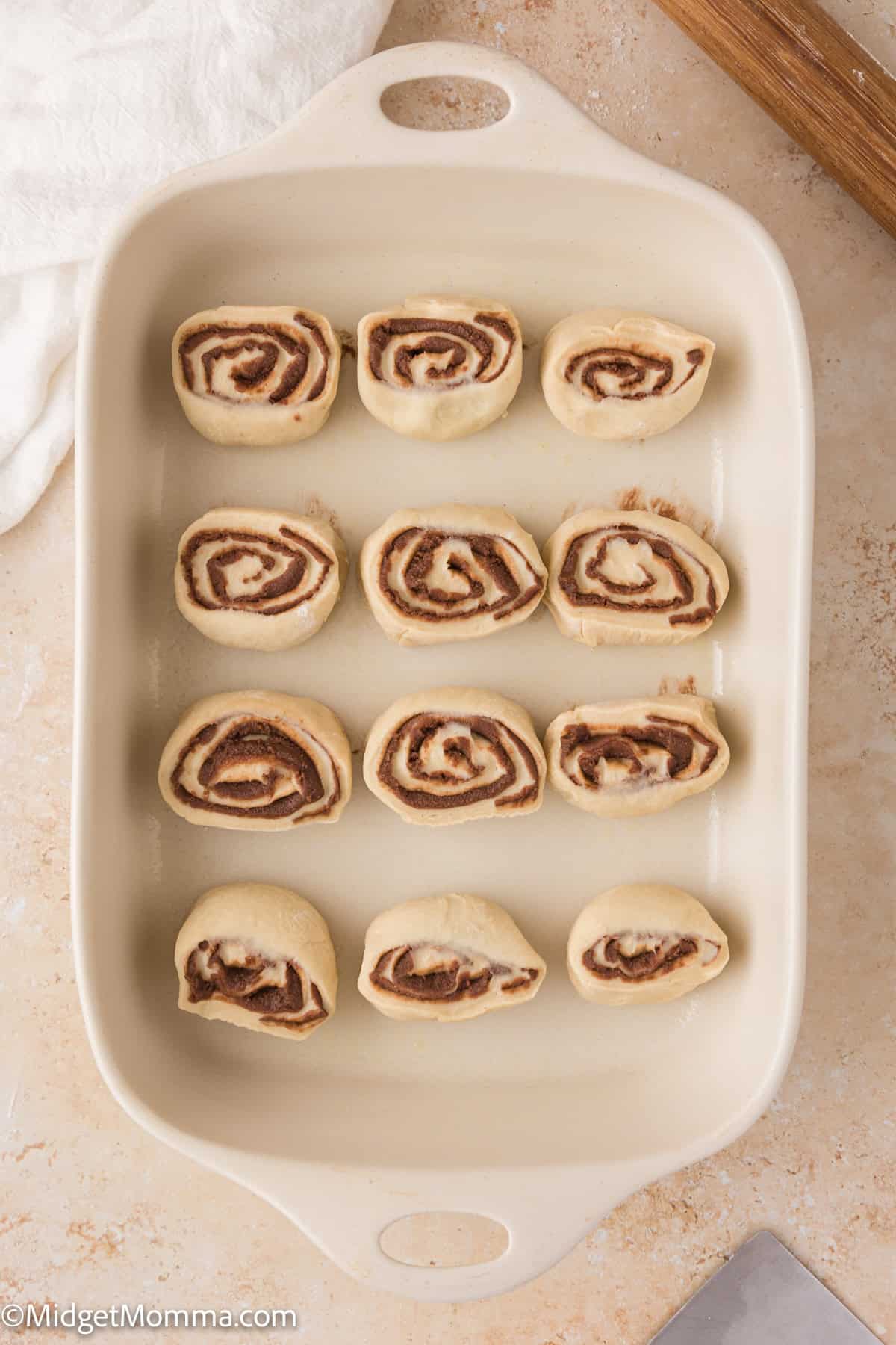 Baking dish with unbaked, sliced cinnamon rolls arranged in rows on a light countertop.