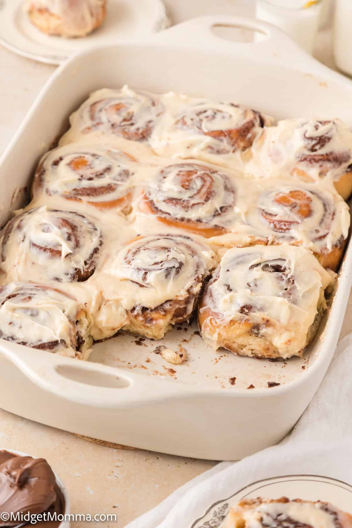 A baking dish with nine cinnamon rolls topped with white icing. One roll is slightly removed from the dish.