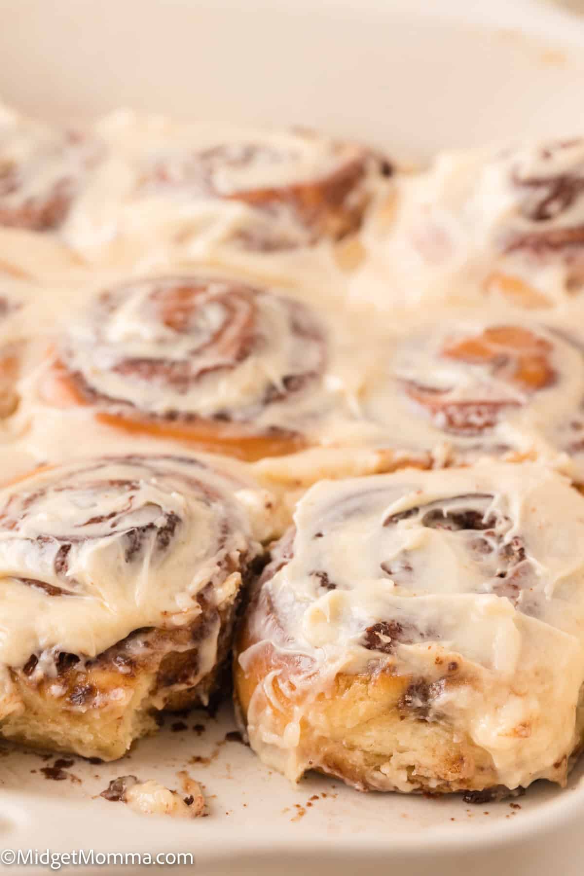 Close-up of frosted cinnamon rolls in a baking dish. One roll is partially removed, revealing a soft, gooey texture.