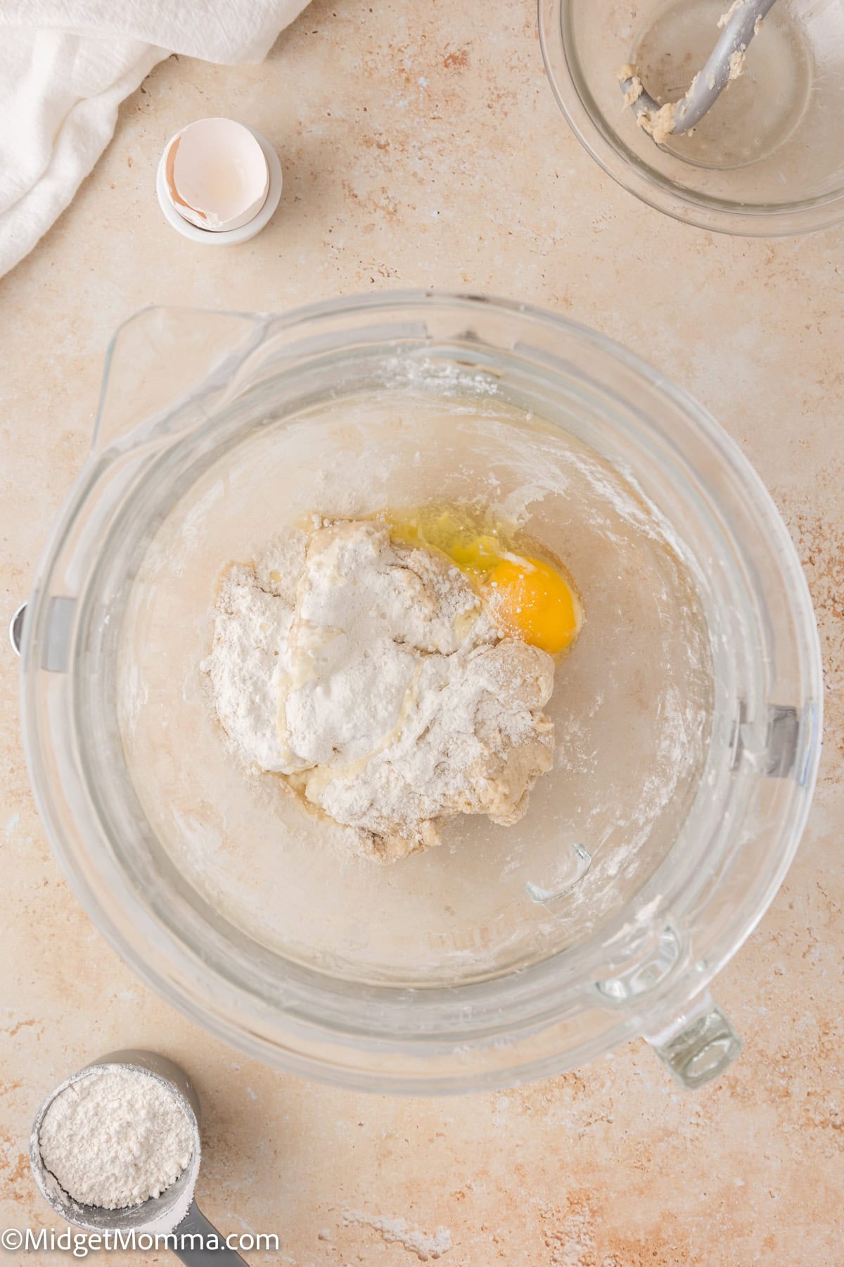 A glass bowl with flour, an egg, and other ingredients for dough on a kitchen countertop.