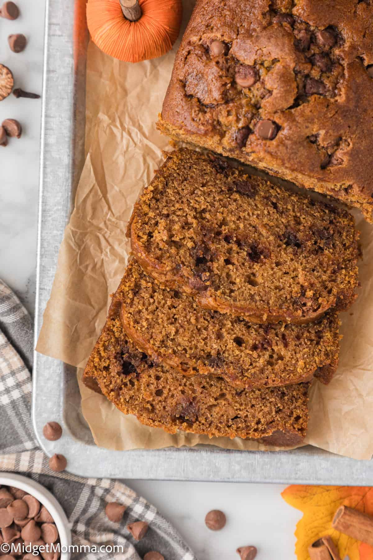 Sliced pumpkin chocolate chip bread on a tray with a small pumpkin in the corner, viewed from above.