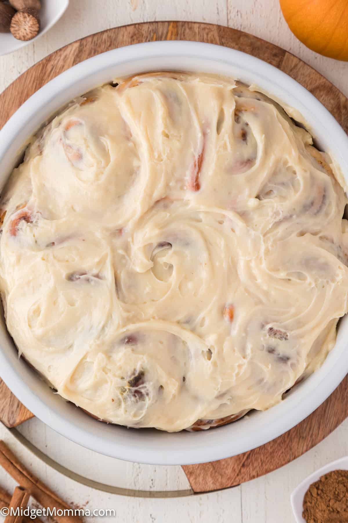 A round tray of cinnamon rolls topped with cream cheese frosting on a wooden board.