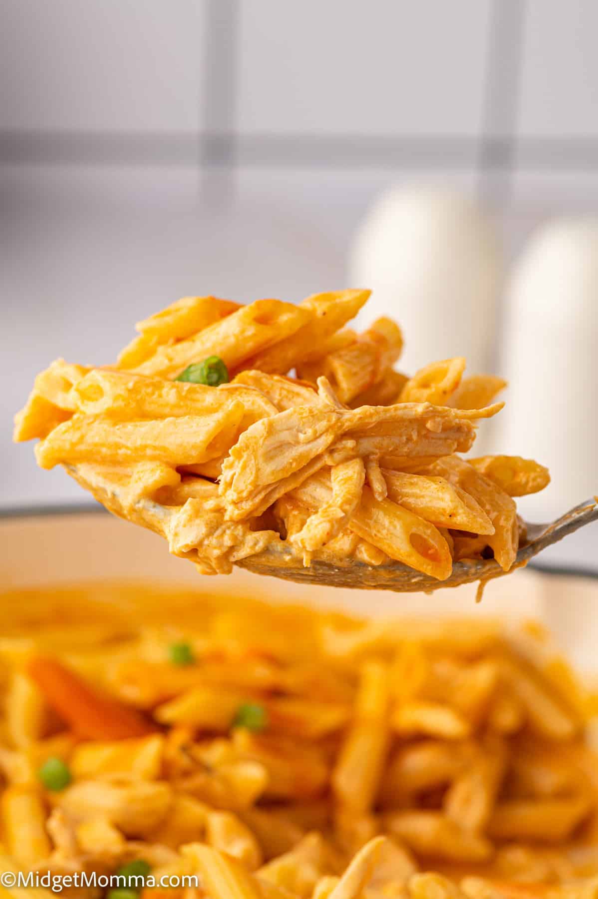 A spoonful of creamy buffalo chicken penne pasta held above a pot.