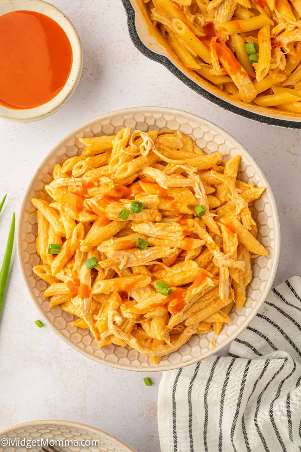 A bowl of buffalo chicken pasta with penne, garnished with green onions, next to a striped napkin.