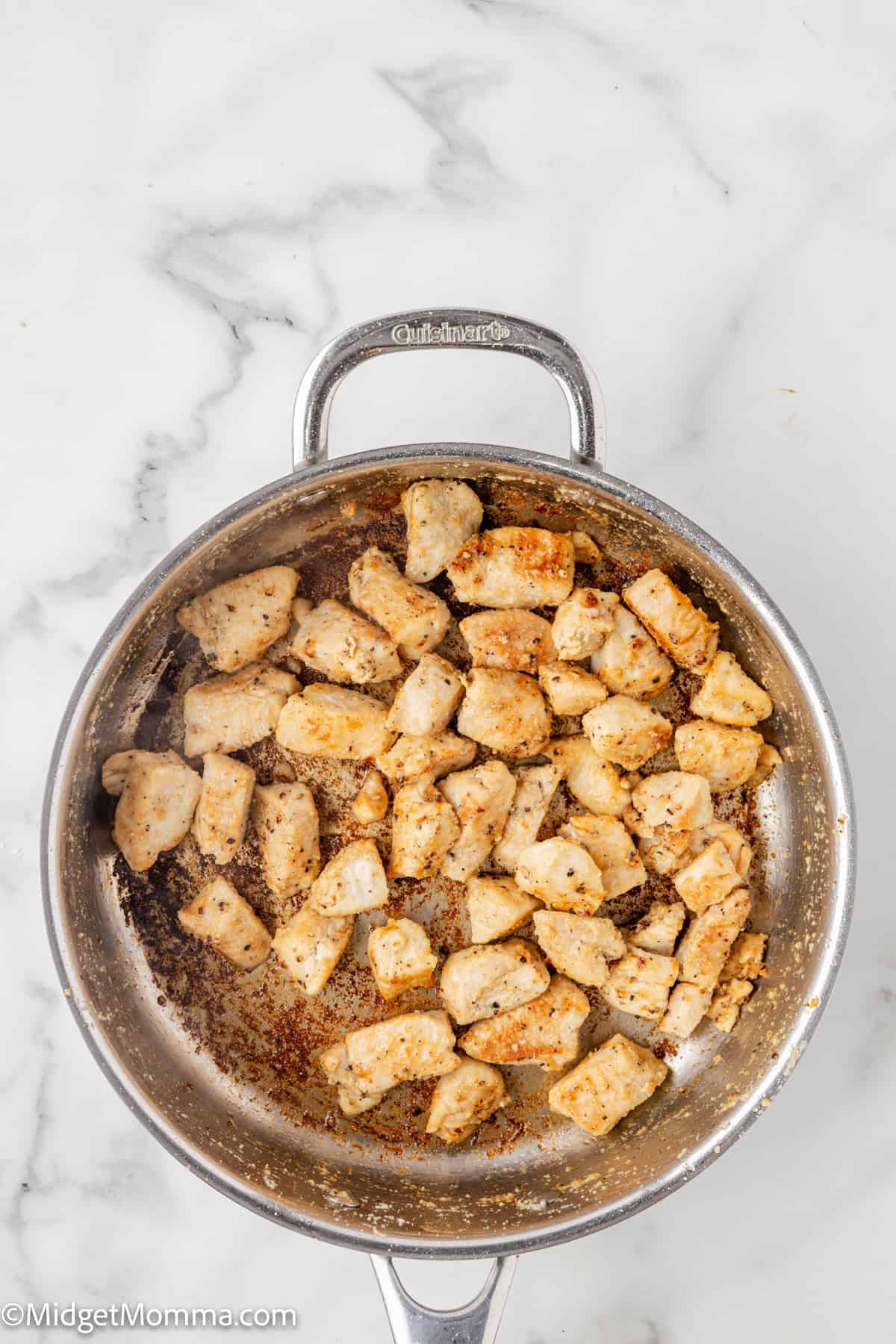 Cooked, seasoned chicken pieces in a stainless steel pan on a marble surface.