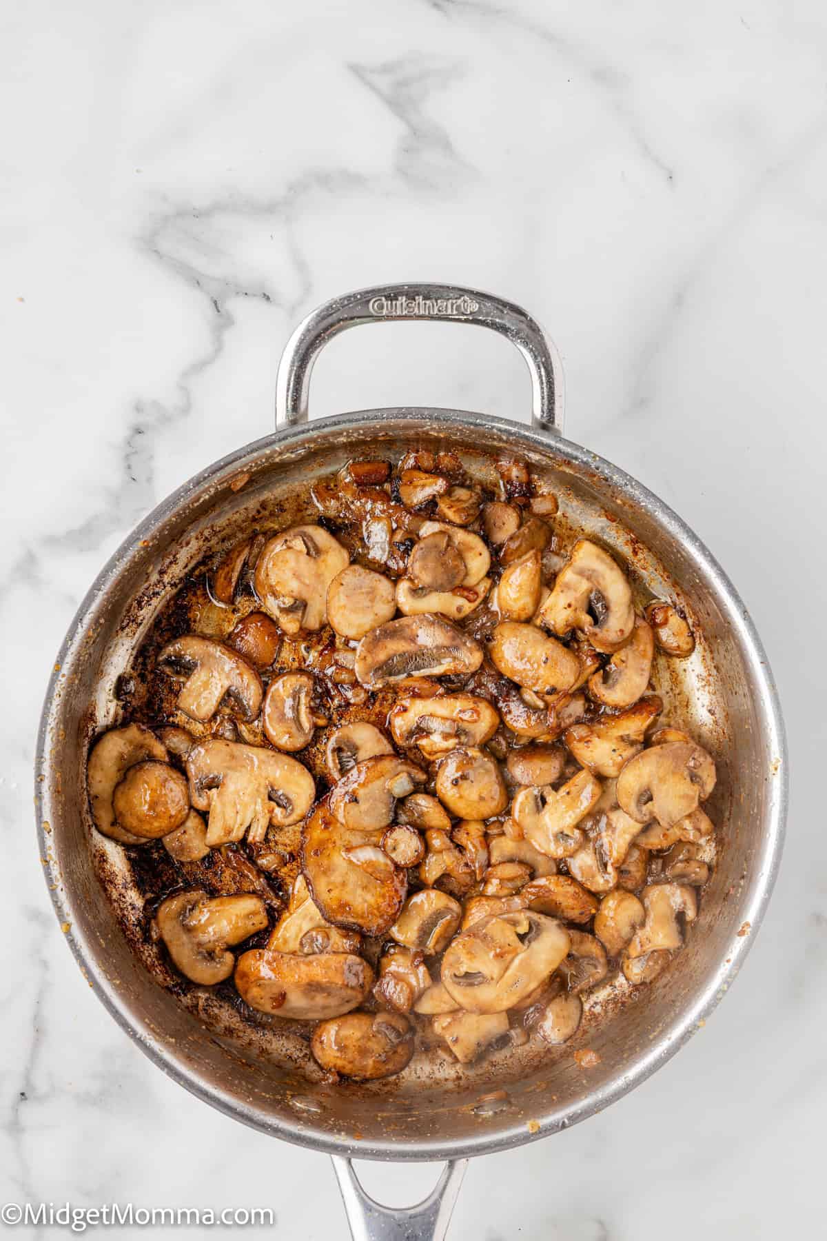 Sautéed mushrooms in a stainless steel pan on a marble surface.