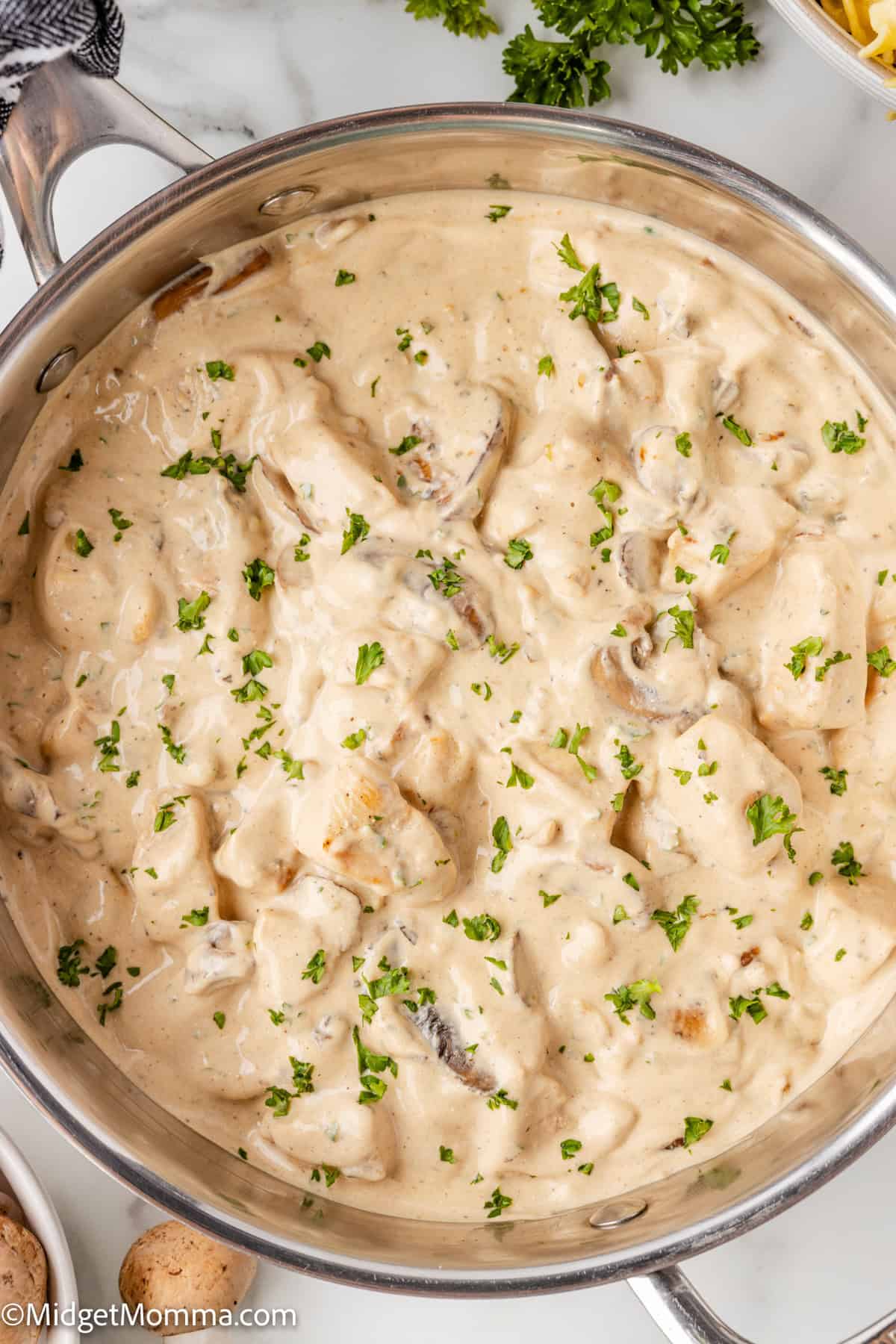 A pot filled with creamy chicken and mushroom sauce, garnished with chopped parsley.