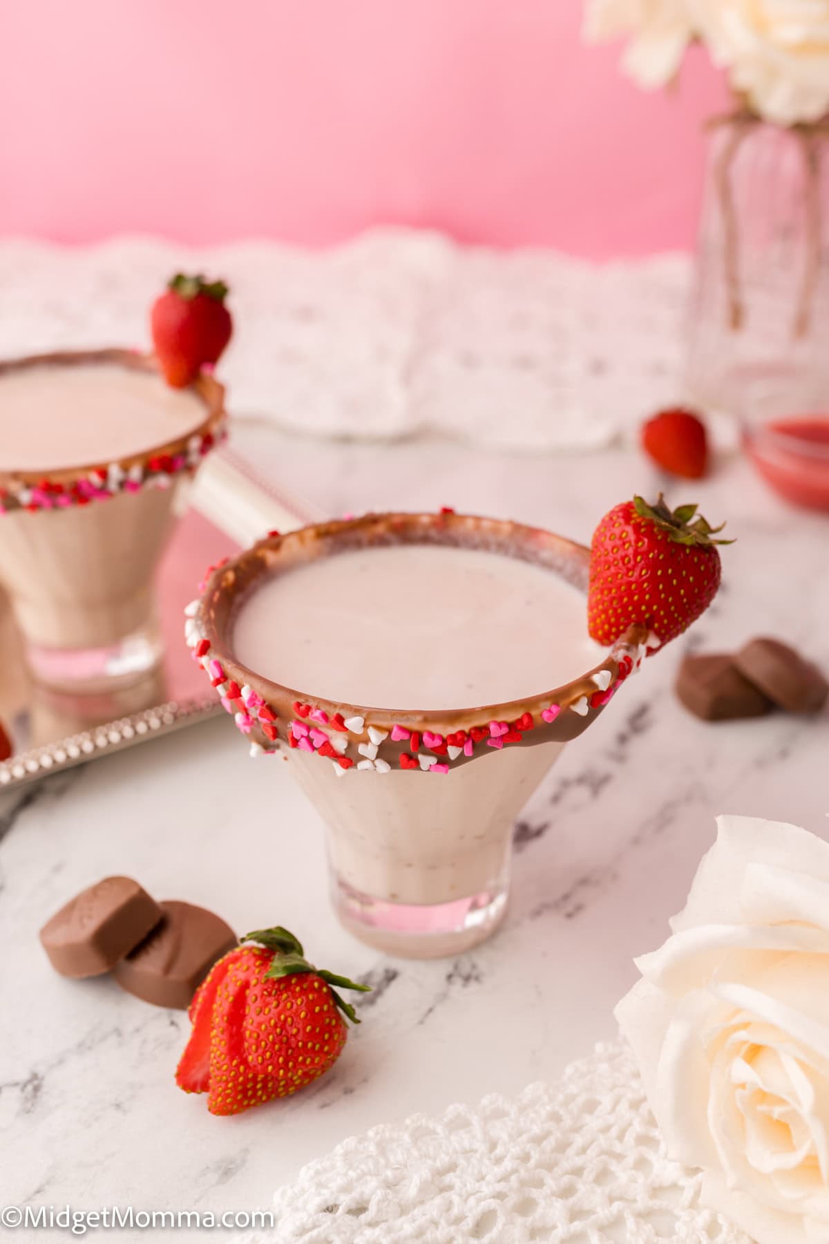 Two strawberry cocktails in glasses with sprinkle and chocolate rim, garnished with whole strawberries, on a silver tray. 