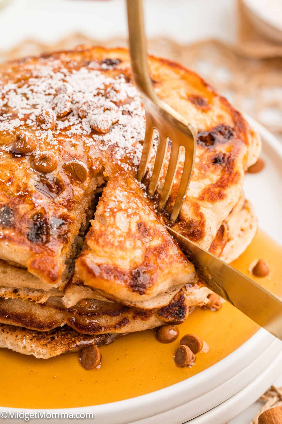 Close-up of pancakes topped with cinnamon chips, powdered sugar, and syrup on a white plate.