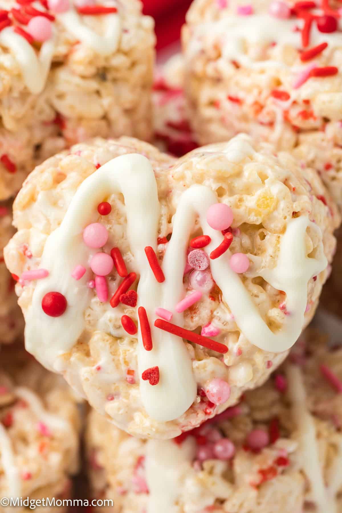 Heart-shaped rice krispie treat with white icing and pink and red sprinkles.